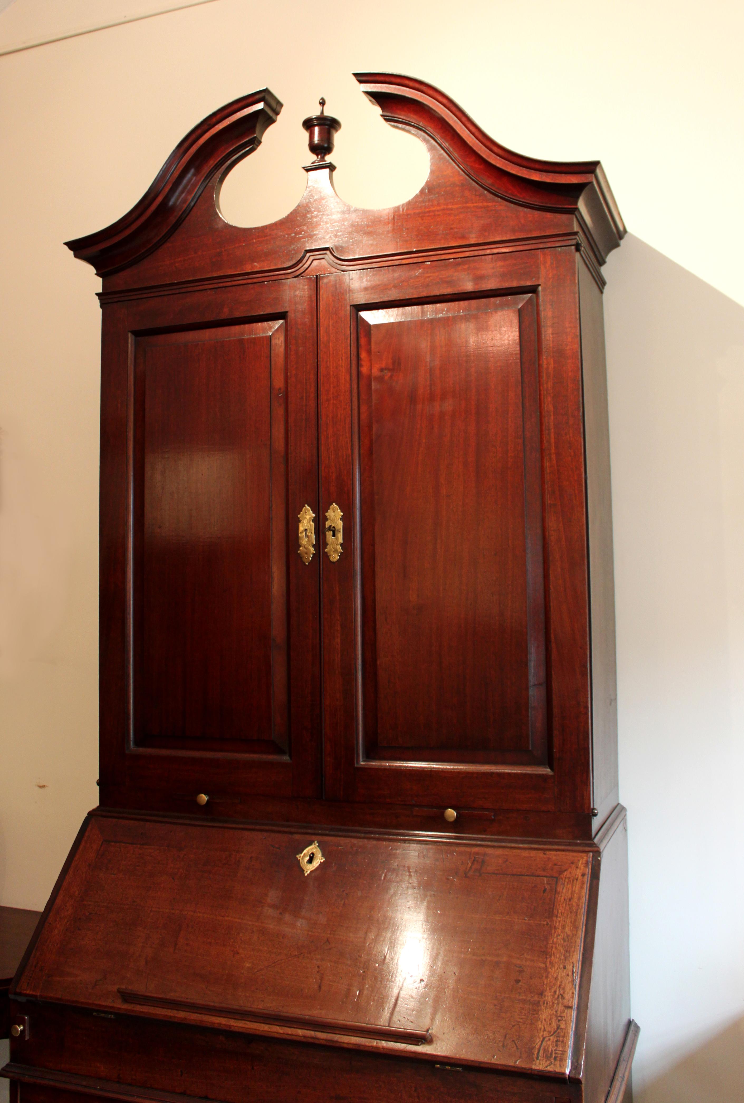 A handsome early Georgian mahogany bureau bookcase with pedimented top; the bookcase section with fielded panel doors and candle slides, the bureau with a well fitted interior, secret drawers, a well and waist moulding