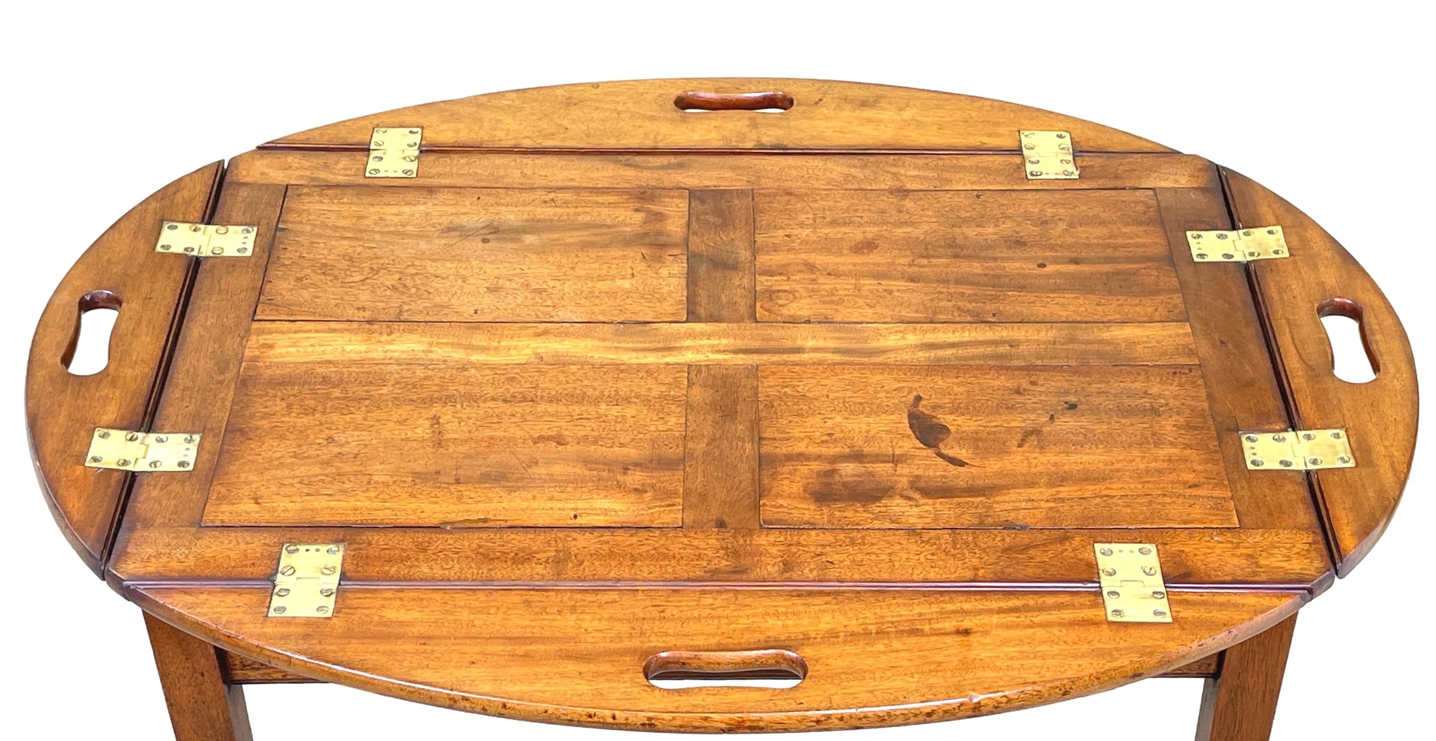 A good quality George III period mahogany oval butlers tray of panelled construction, having original brass hinges and pierced handles to folding sides, housed on later square leg mahogany stand.


During the 18th and 19th centuries a coffee