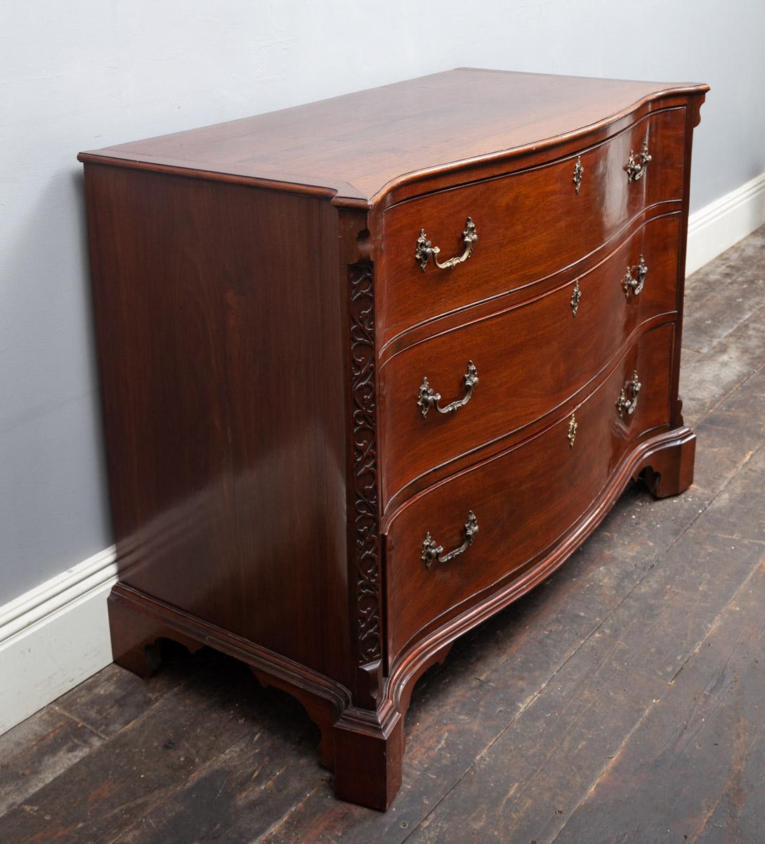 A very fine 18th century mahogany serpentine chest of drawers in the manner of Thomas Chippendale. The beautifully figured and patinated serpentine moulded top, with canted corners above three serpentine drawers, each with gilded Rococo handles and