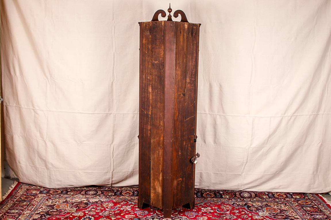 Georgian corner cabinet, mahogany, canted corners, a carved broken bonnet top with rosette ends and a ball and spike finial, upper cabinet panelled inside with three shaped shelves, a glass door with mullions and a satinwood escutcheon with key,