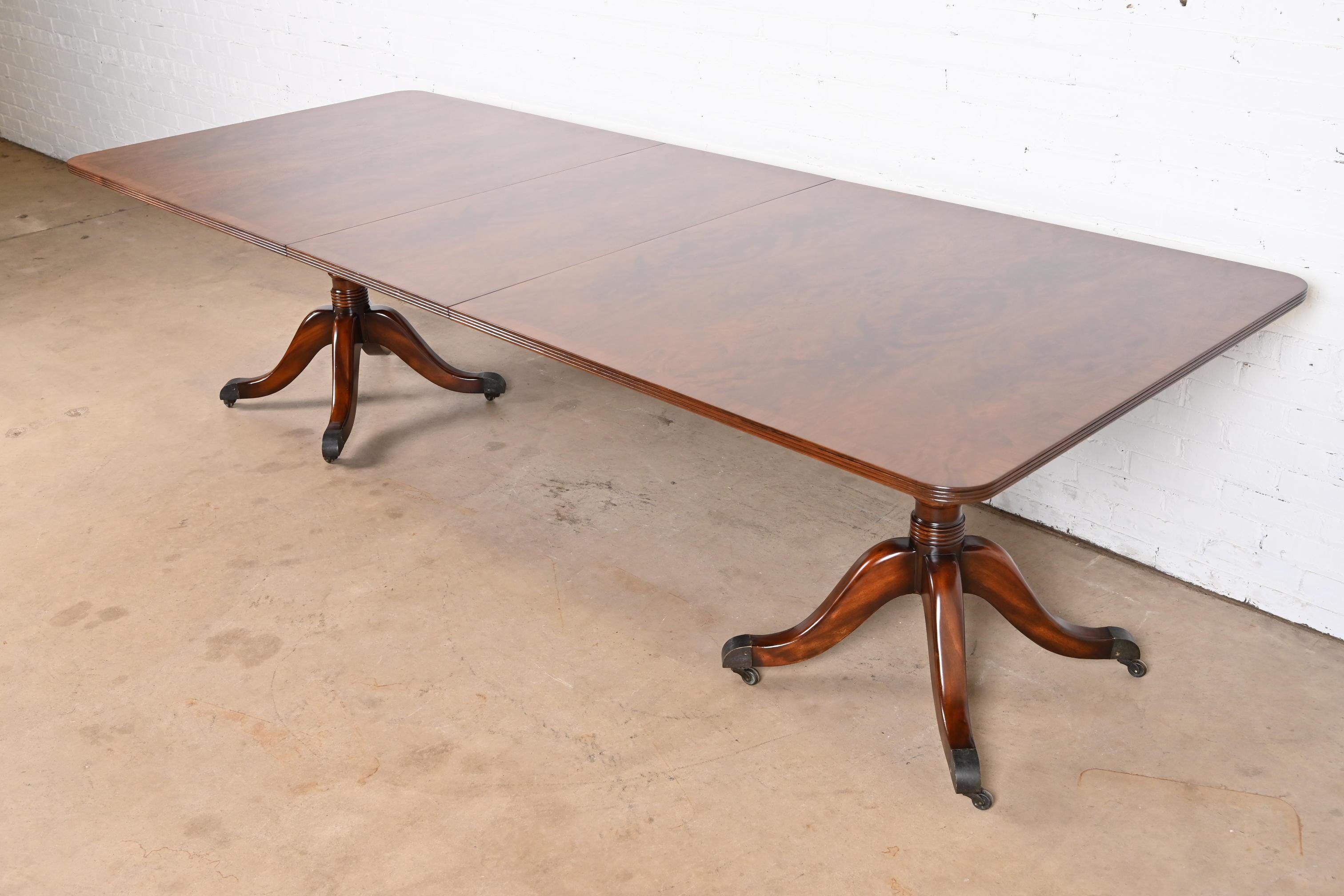 A gorgeous Georgian or Regency style double pedestal extension dining table

In the manner of Baker Furniture

USA, Circa 1980s

Stunning book-matched banded mahogany, with carved solid mahogany pedestals, and brass capped feet on