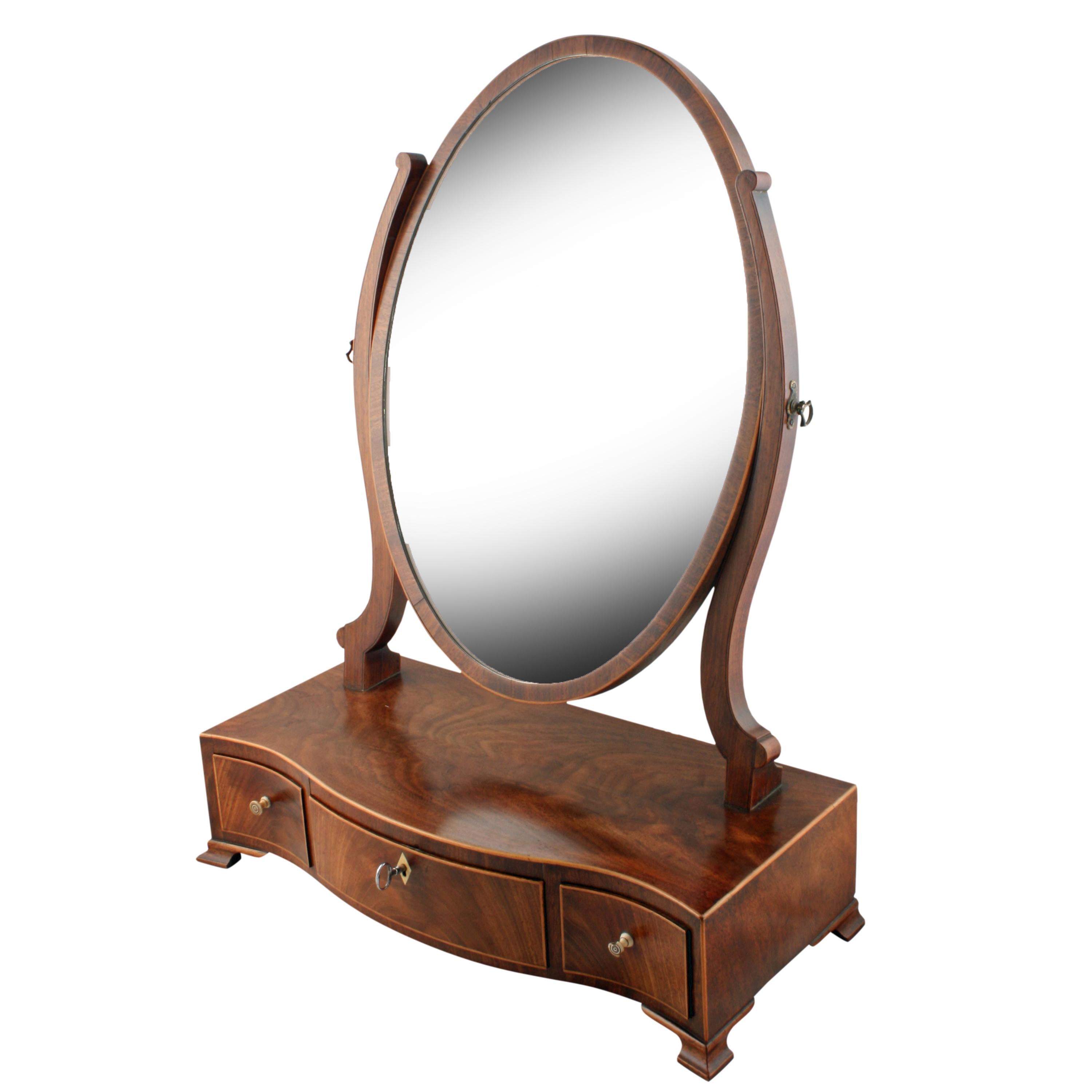 A late 18th to early 19th century Georgian mahogany three-drawer dressing mirror.

The mirror plate is in a mahogany frame with a box wood edge that is held between two shaped arms and rotates on a pair of brass knobs.

The serpentine shaped