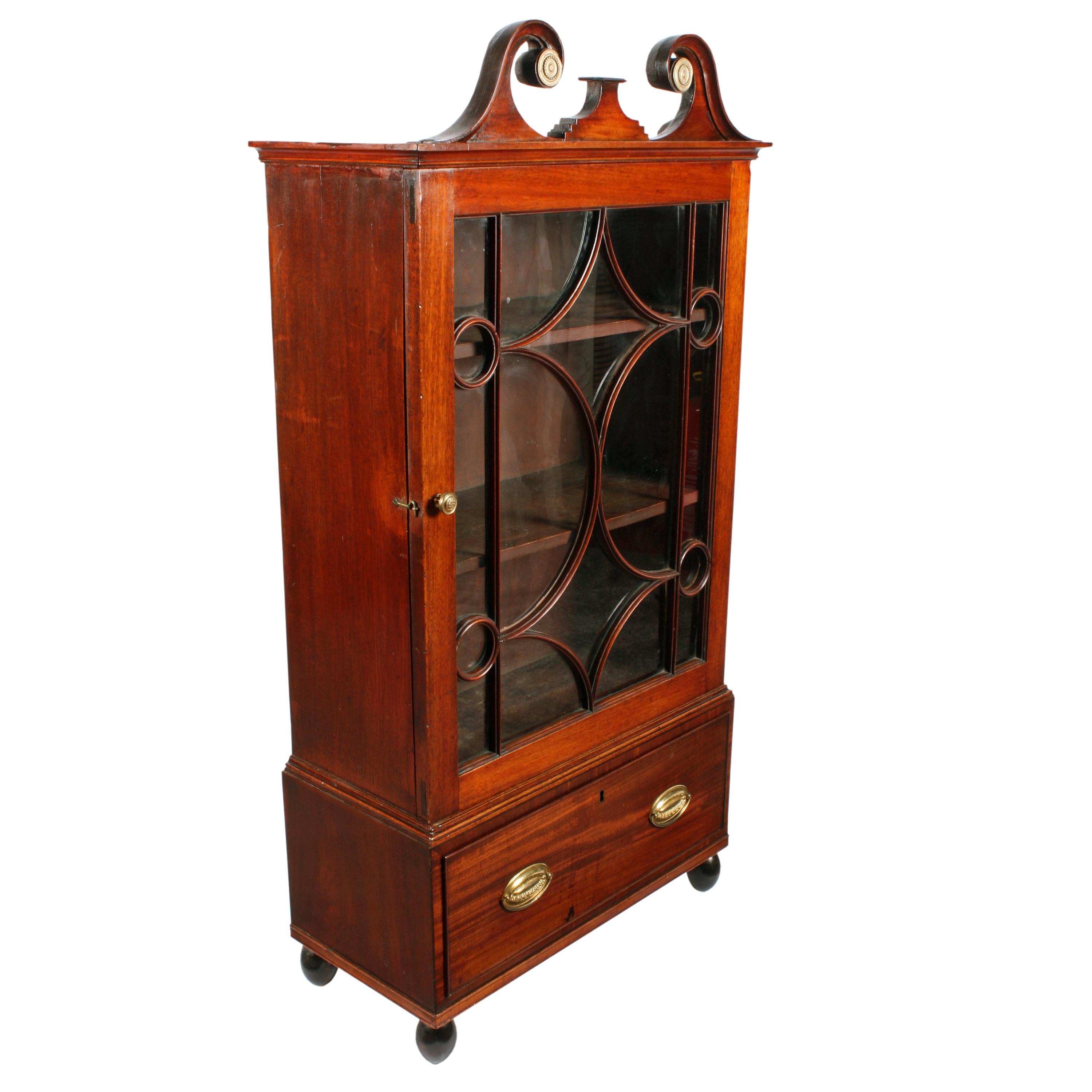 An early 19th century Georgian mahogany dwarf cabinet.

The cabinet is of small proportions with a single glazed door, a drawer, a bold swan neck pediment and stands on turned ball feet.

The door has geometric glazing with eighteen panes of