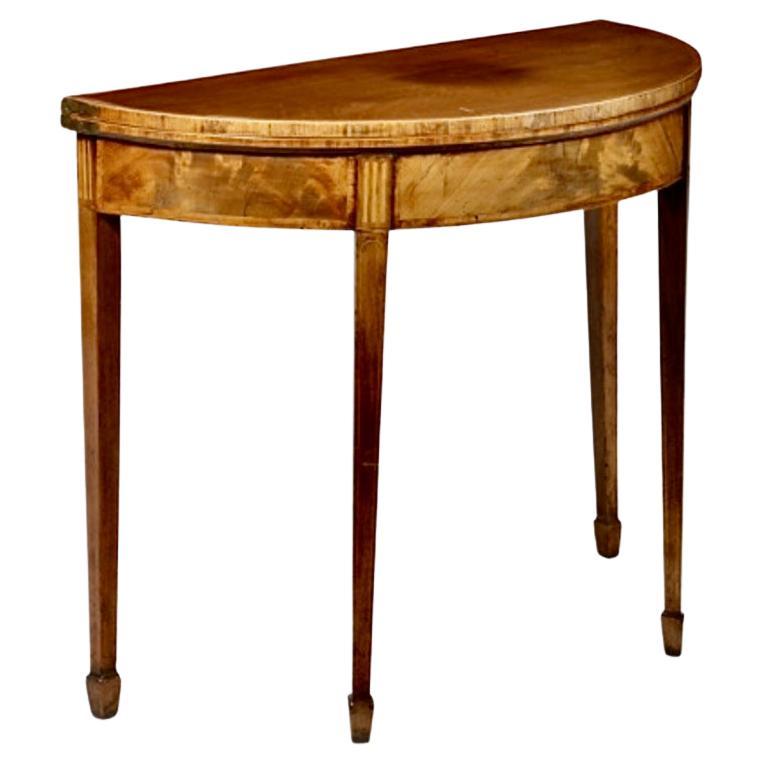 This is a good example of a classic George III Fold-Over Games Table. The table features a solid mahogany top and a beautifully figured mahogany skirt detailed with line inlay and an inlaid fluting surmounting the four line inlaid  legs with spade