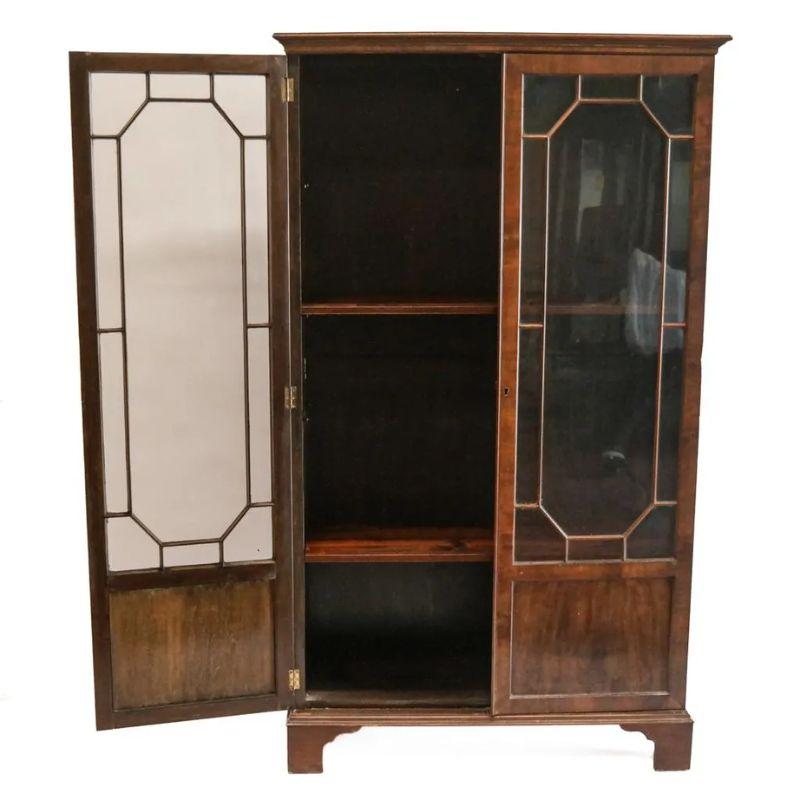 A vintage mahogany, Georgian style tall cabinet with glass doors. The glass on each door has octagonal molding for a divided light design and recessed panels at the bottom. The wood shows beautiful grain. The cabinet is finished with traditional