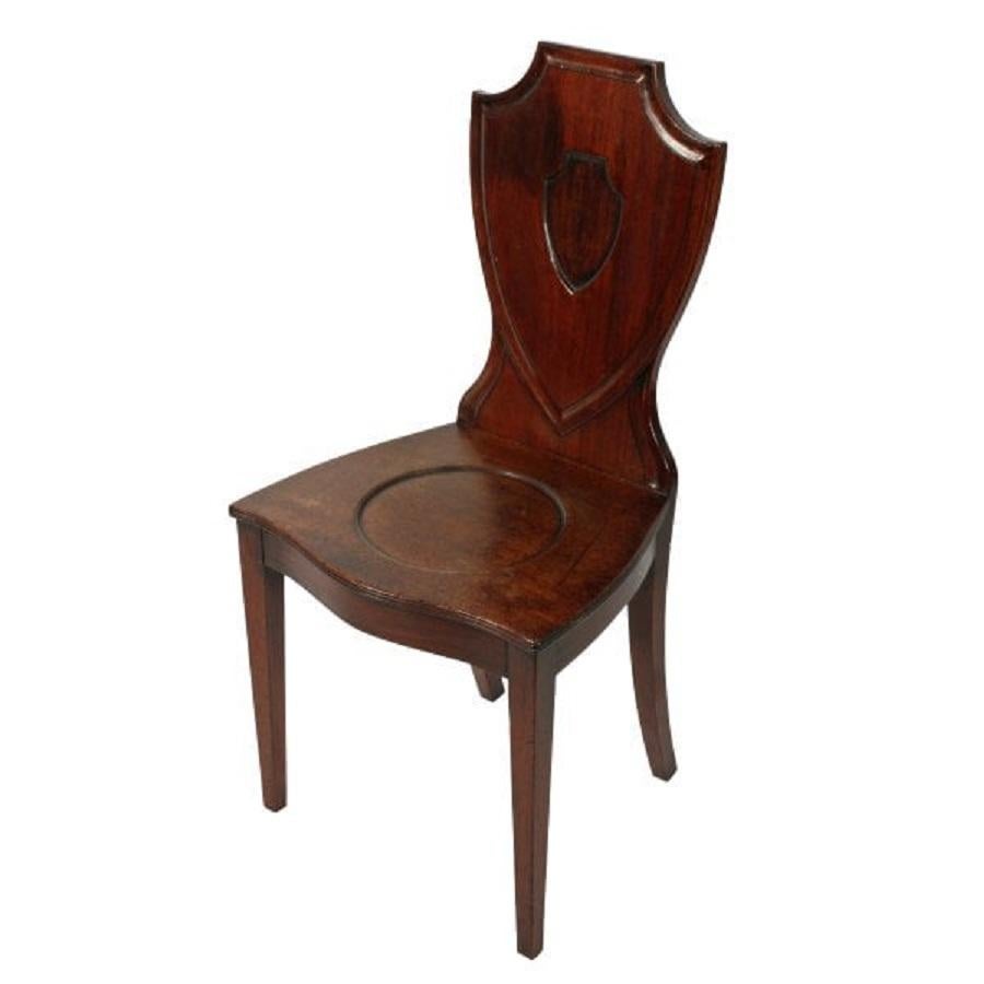 An 18th century Georgian mahogany hall chair.

The chair has a shield shaped back, a mahogany seat with a serpentine front, a reeded edge and a decorative circle turned in the seat.

The shield shaped back has a recessed carved shield cartouche