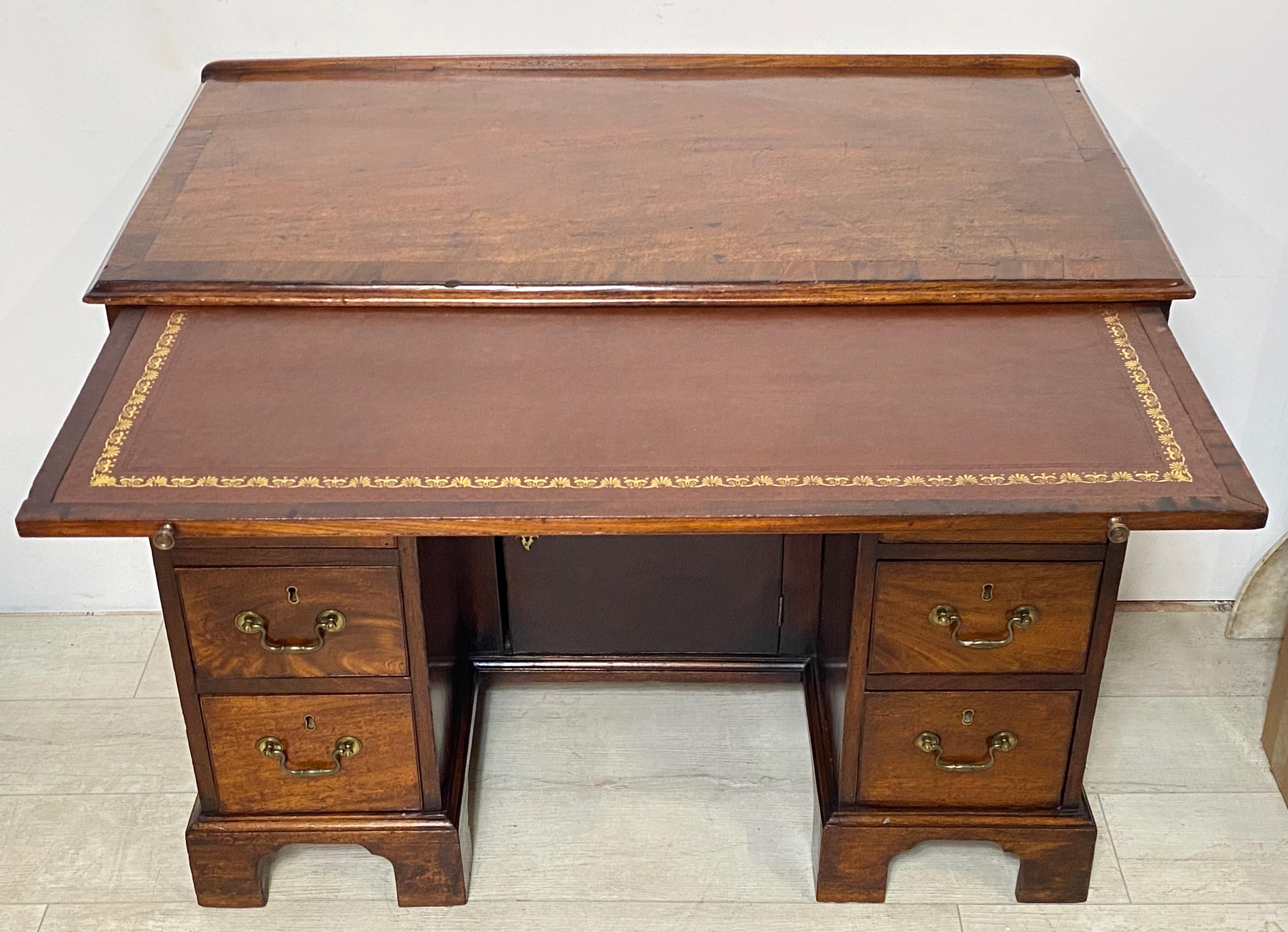 Georgian period mahogany kneehole desk with inset leather slide writing surface decorated with gilt tooling. Having a single full width center drawer over a hinged cupboard door at the center within the kneehole, flanked on either side by three