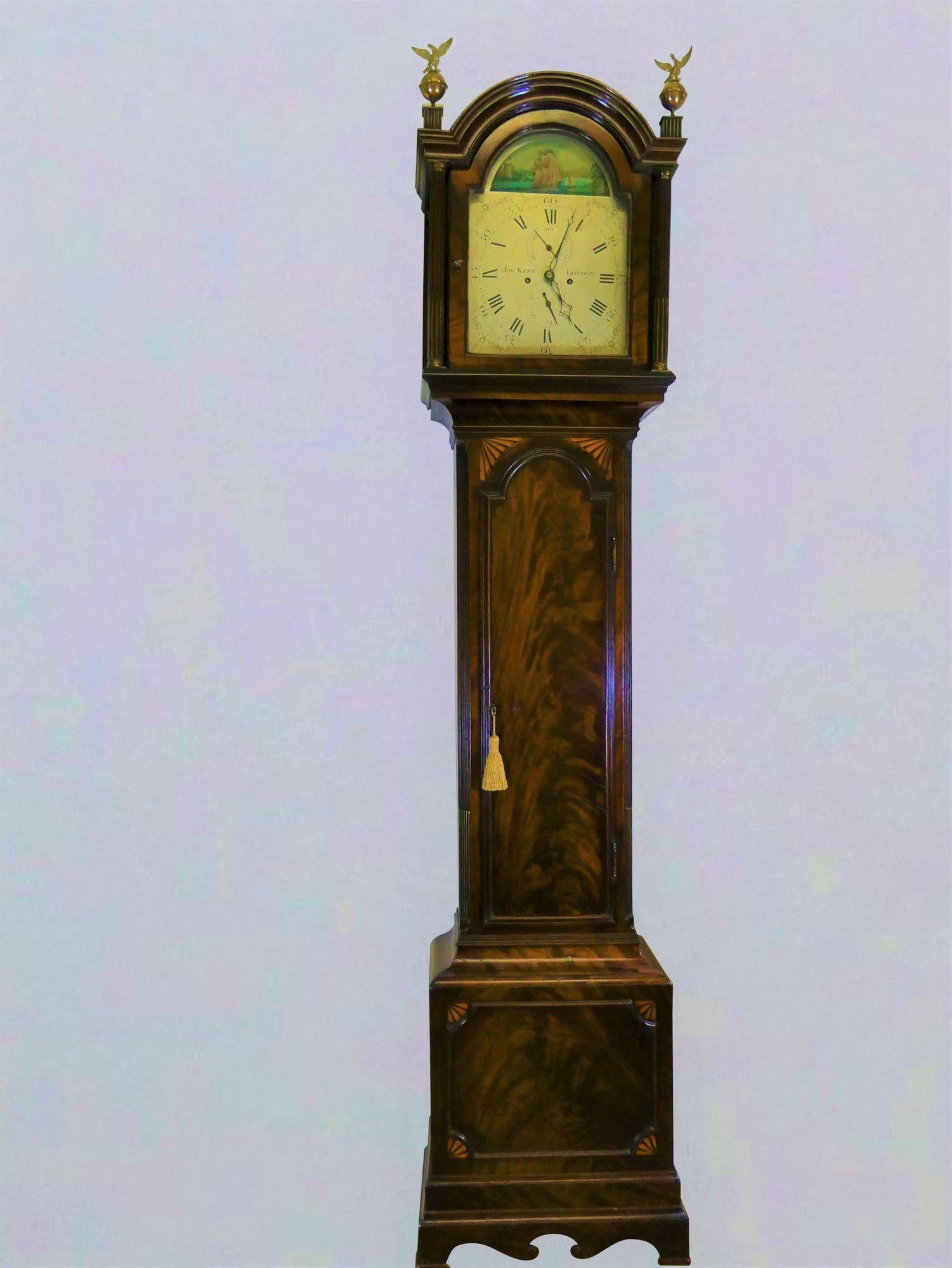 Georgian Mahogany Longcase Clock with Rocking Ship Automation, Joseph Kent, London.
 
Fine flame mahogany case with break arch hood, reeded pillars with brass capitals to either side of the glazed door surmounted by two brass finials.
Long break