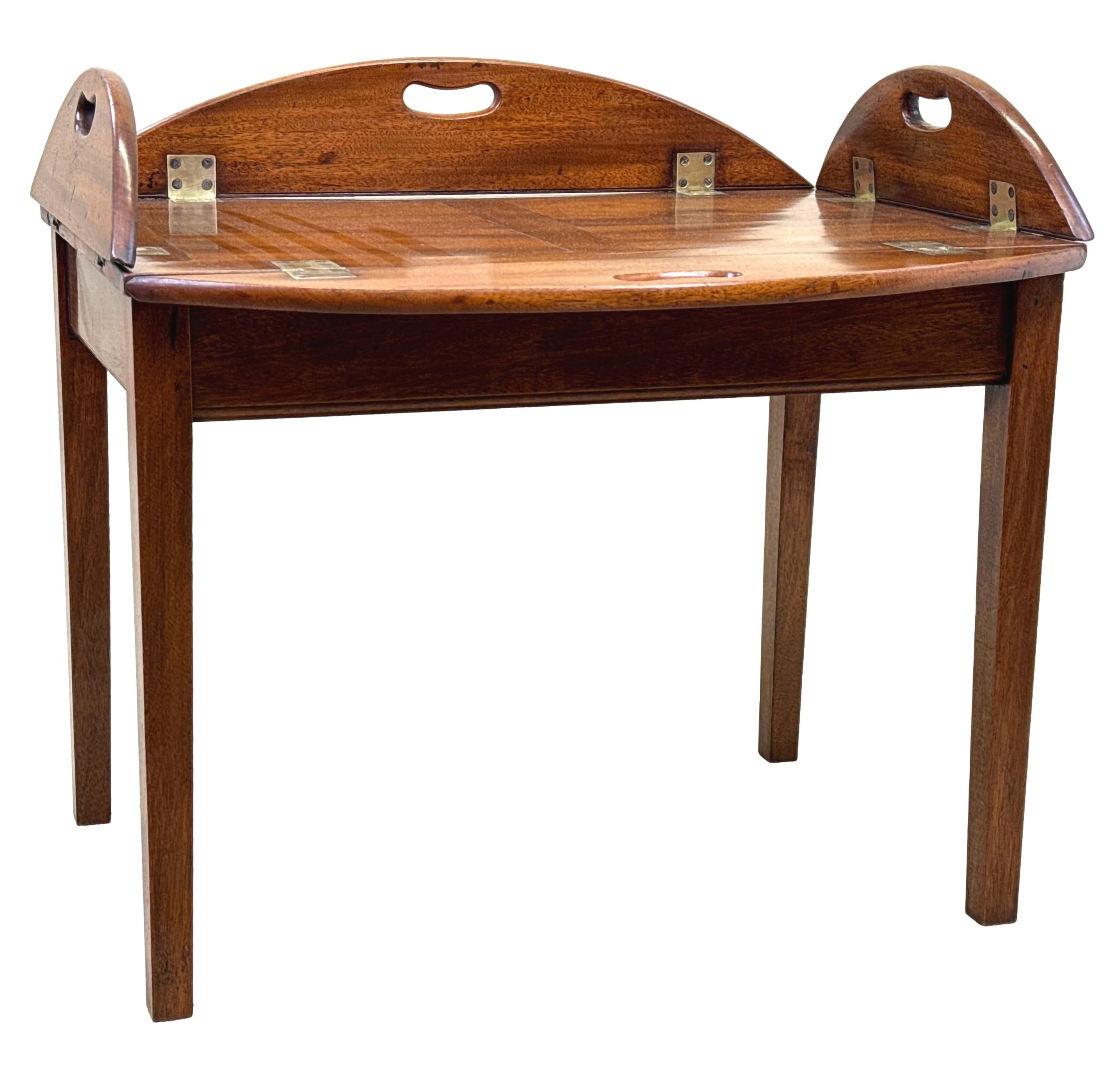 A Very Good Quality George III Period Late 18th Century Mahogany Oval Butlers Tray, Of Typical Four Panel Construction, With Original Brass Hinges To Folding Sides With Pierced Carrying Handles, Raised On Later Square Tapered Leg Stand.


During the