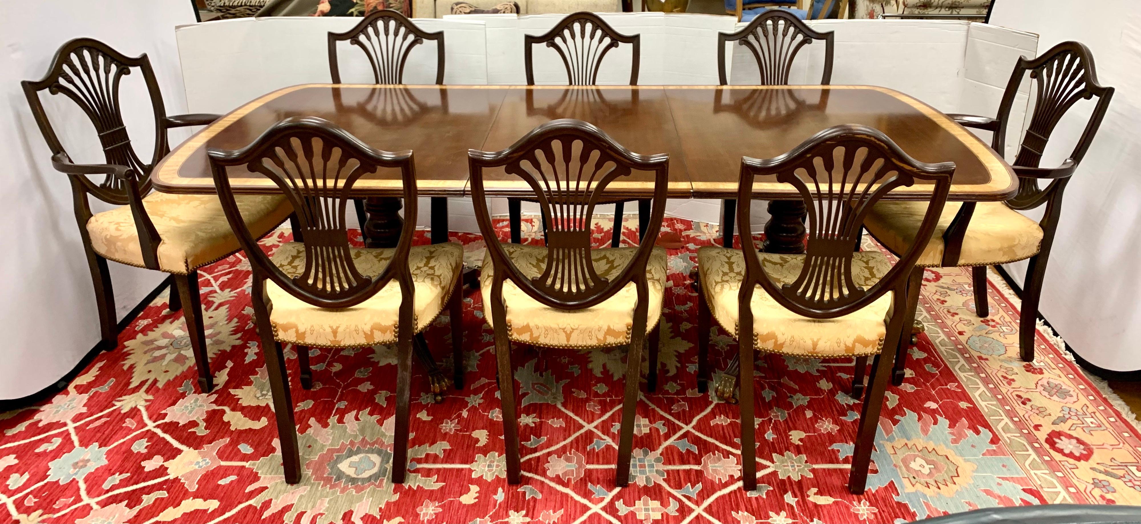 Classic traditional 9 pc. dining set includes a mahogany inlay double pedestal dining table and 8 shield back chairs, 2 arms and 6 side, with carved classical wheat sheaf motifs along the pierced splats. All on square tapered legs. Upholstery is in