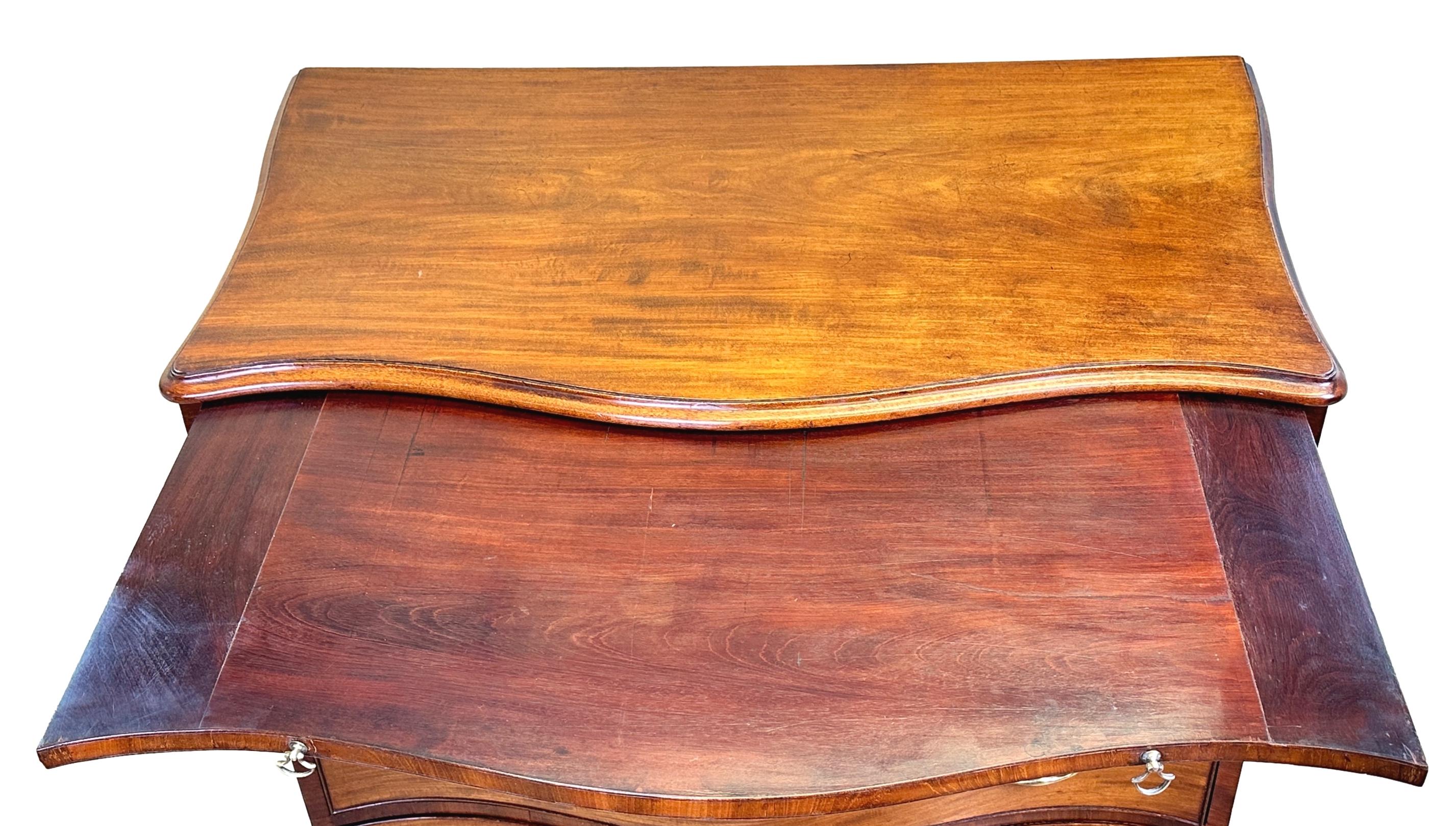 A Very Good Quality Late 18th Century, Georgian, Mahogany Chest, Of Elegant Serpentine Form, Having Well Figured Shaped Top Over Brushing Slide And Four Long Drawers, Retaining Original Brass Swan Neck Handles And Raised On Original Shaped Bracket