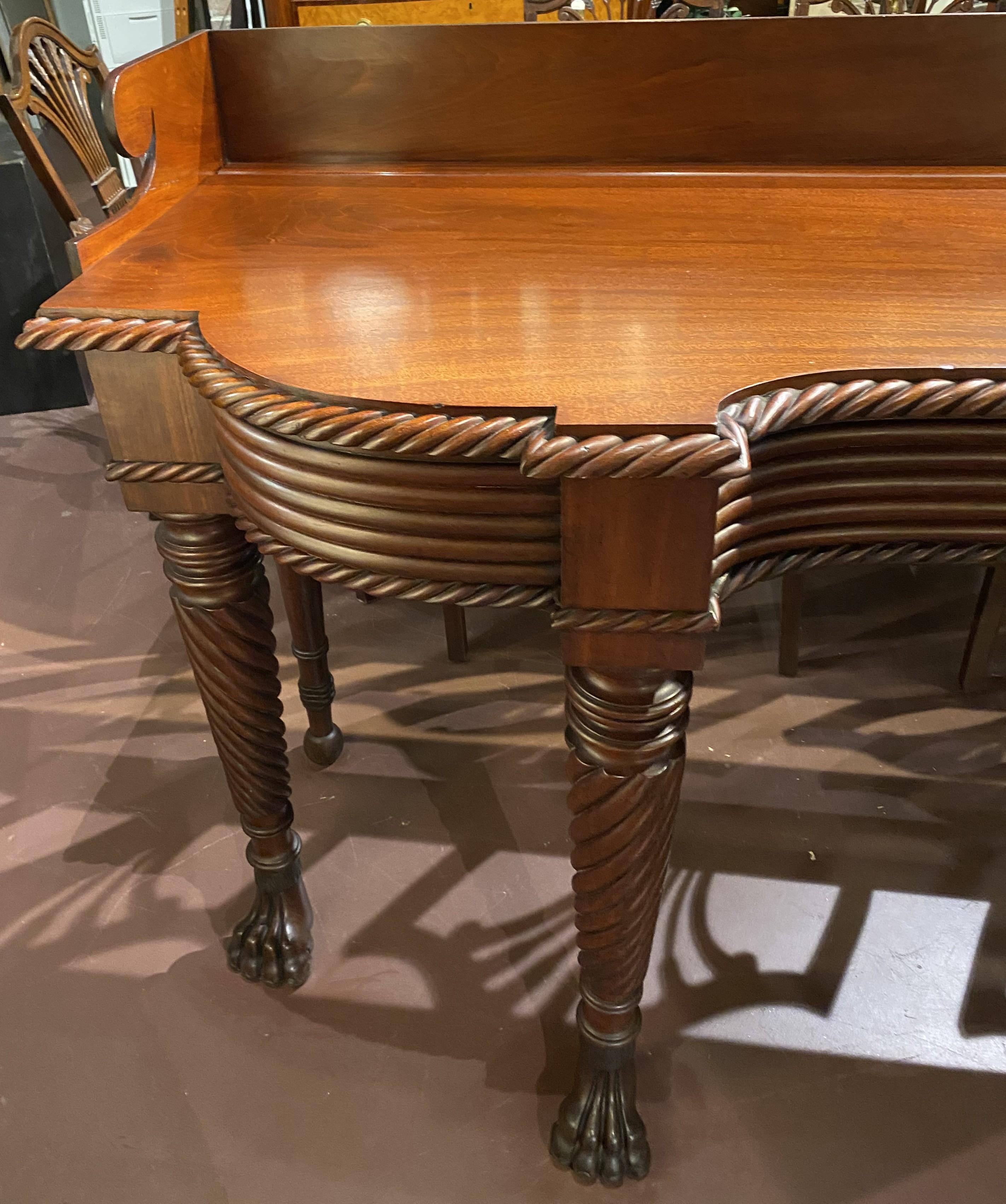 A wonderfully carved English Georgian mahogany server with shaped splash rail and gadrooned edge top, featuring a side drawer and set back top, constructed to conform to a chair rail, all supported by four rope turned front legs, terminating with