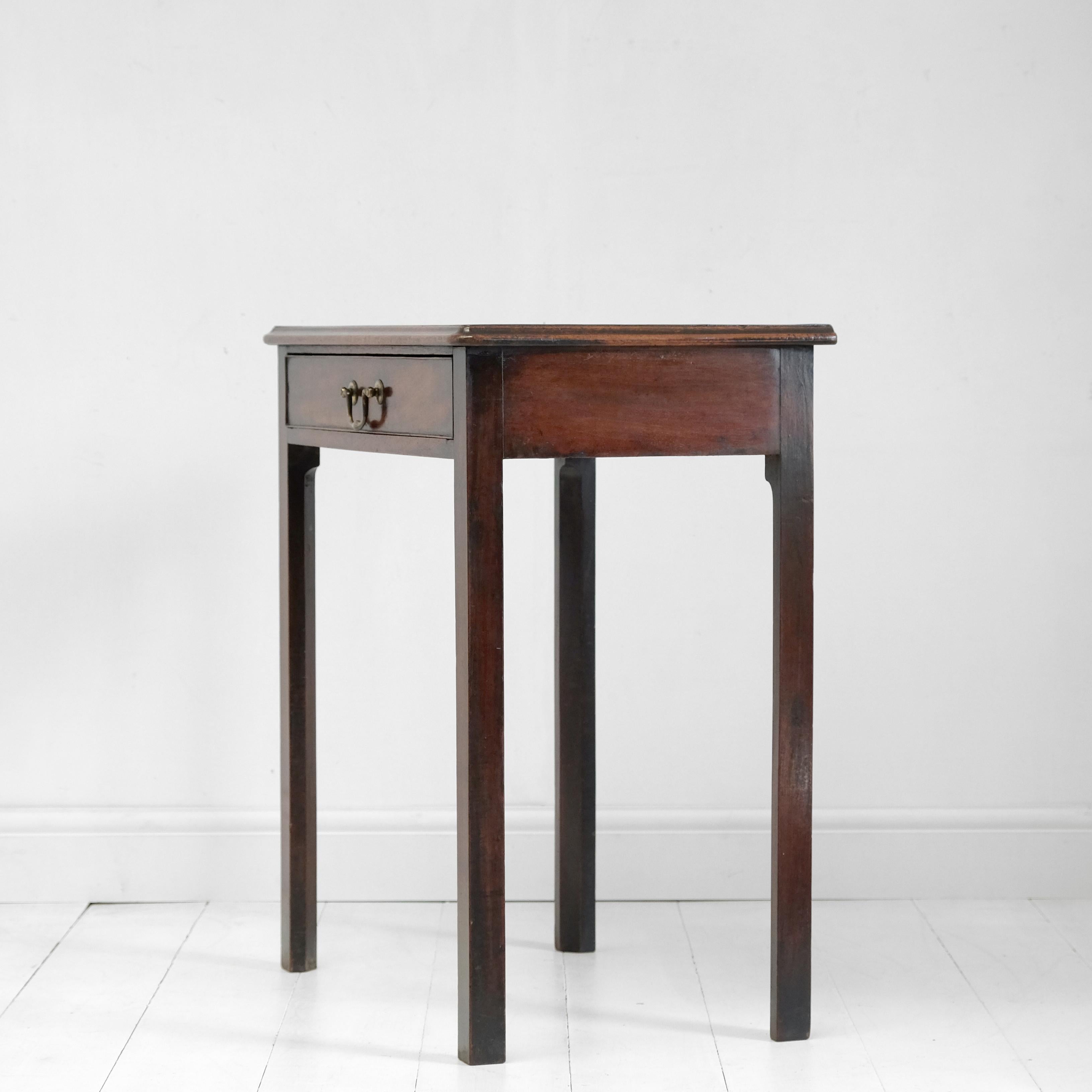 A diminutive Georgian side table in mahogany. In original condition with a lovely warm color and patina. Original swan neck brass handle to the oak-lined drawer. Simple chamfer-cut square legs with moulded top above. English, circa