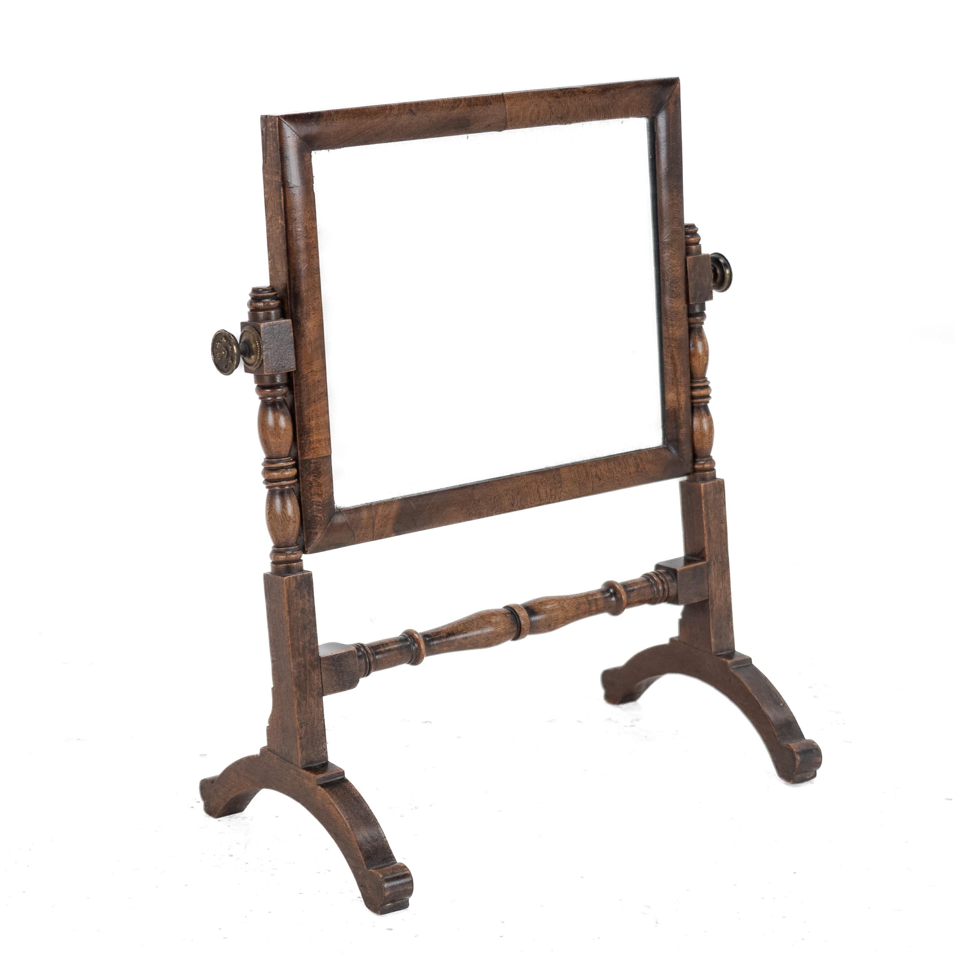 A George III period, mahogany framed toilet mirror, circa 1800. This original tabletop vanity mirror in solid mahogany with brass locking knob handles. Original oblong mirror plate with cushion moulded frame. Wood panelled back. The mirror angle can