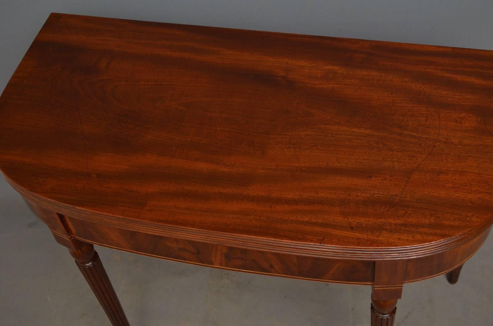 J00 elegant George III tea table in mahogany, having figured mahogany fold over top with reeded edge and flamed mahogany frieze with satinwood inlays, standing on slender, reeded and tapered legs. This antique table has been sympathetically restored