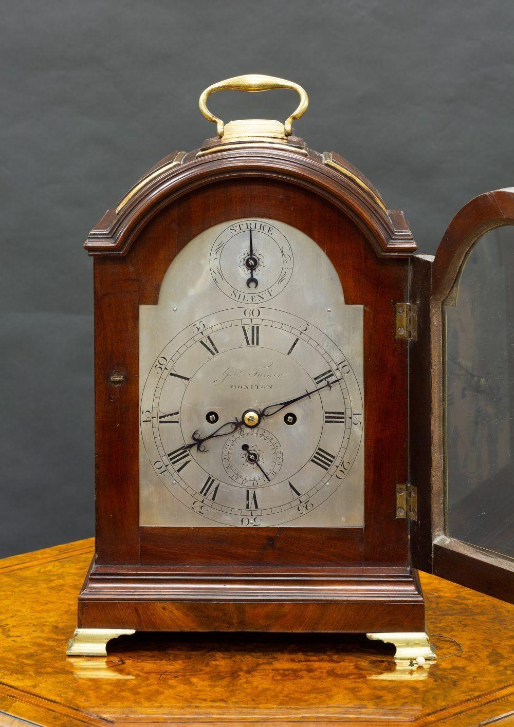 Georgian Bracket Clock
Mahogany brass bound case standing on a raised stepped plinth and resting on brass bracket feet with silk lined fishscale sound frets surmounted by a break arch with three brass bound pads with central mounted carrying