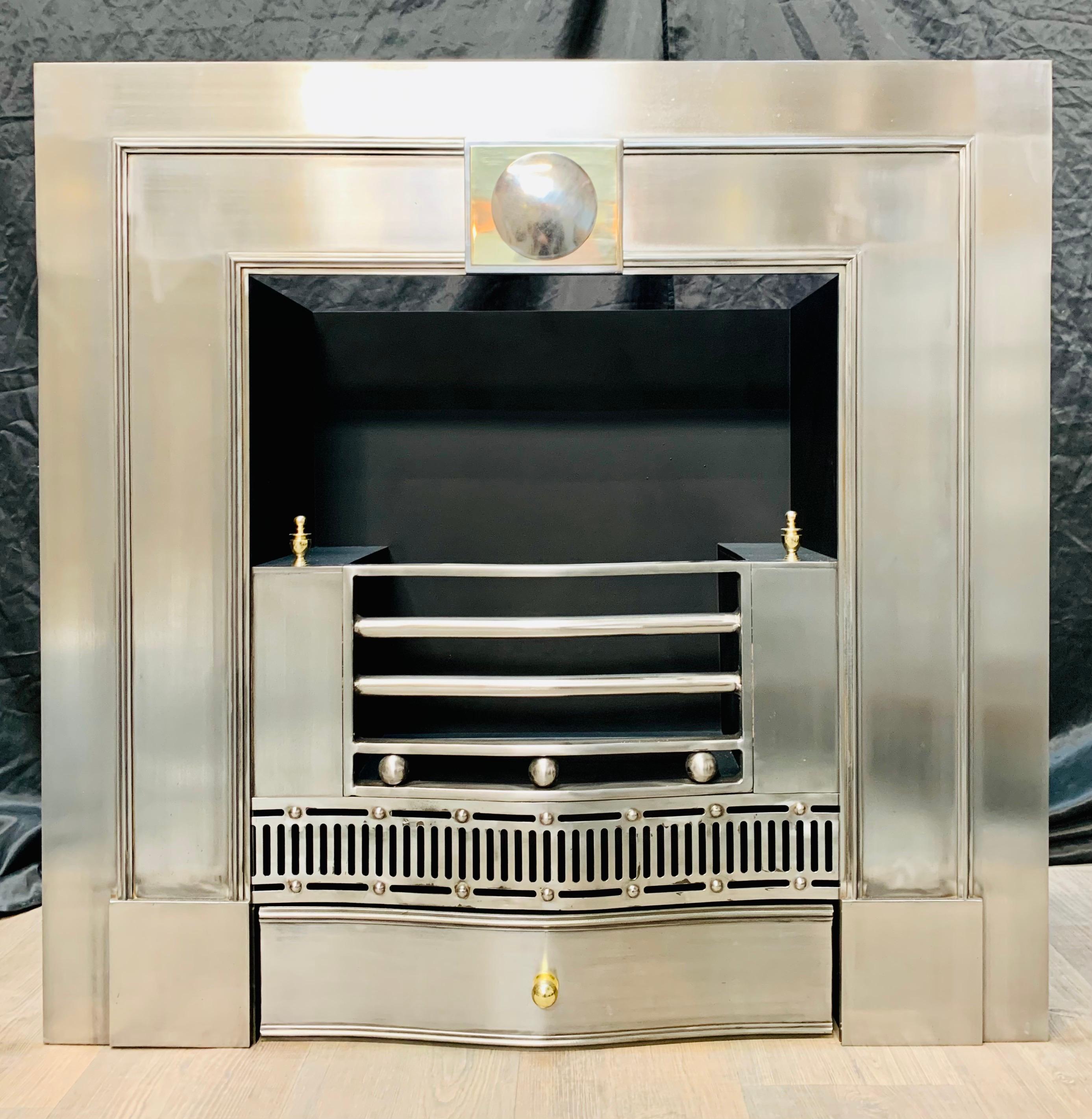 A charming and versatile polished steel fireplace insert in the Georgian manner. A generous outer plate displaying a central tablet with a polished brass mount and a polished steel disc, a three barred polished fire front with side cheeks, above a