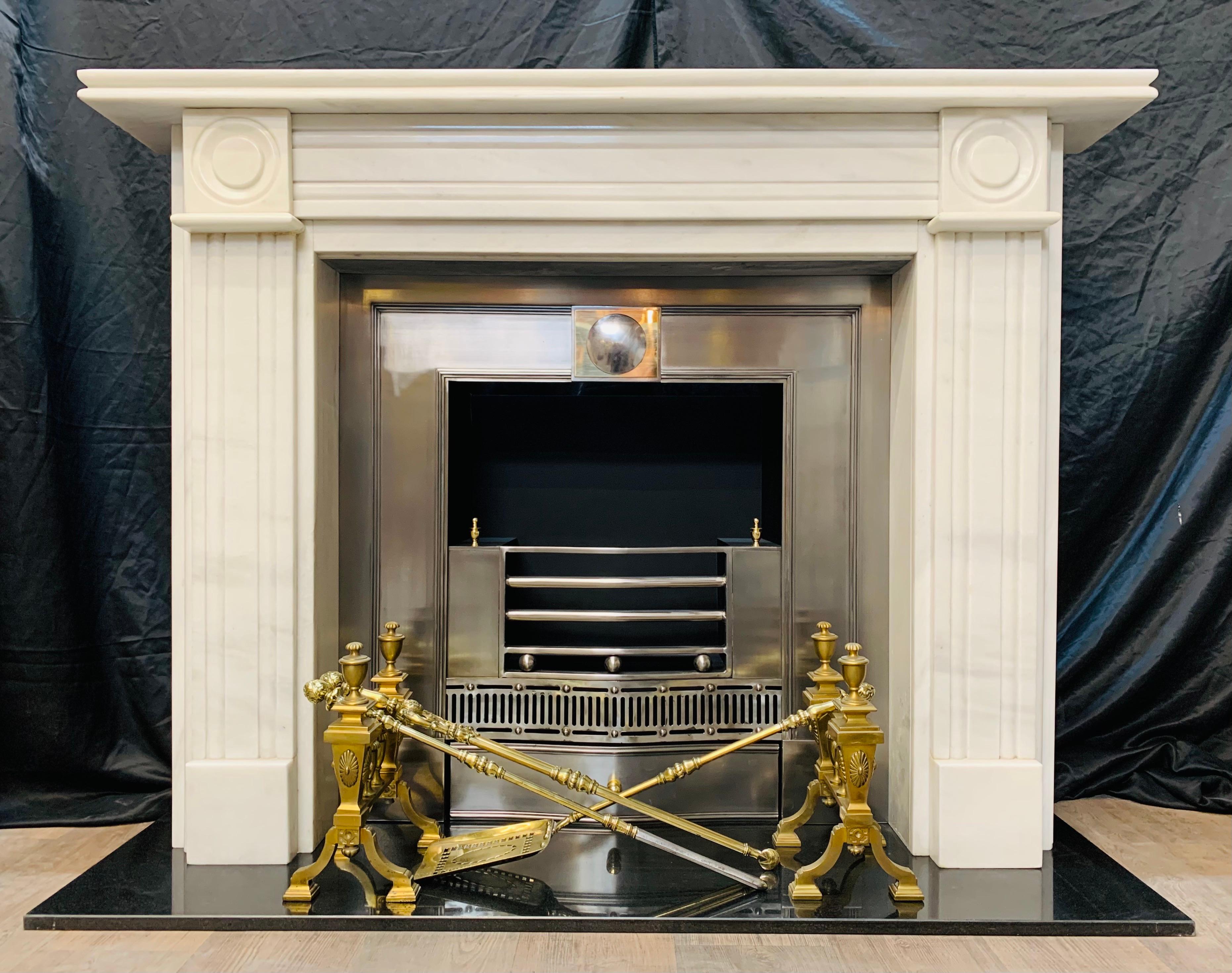 A substantial lightly veined white marble bullseye fireplace surround in the Georgian manner. A double corvetto moulded shelf rests above a moulded and channeled frieze, flanked by a pair of bullseye capitol's- below a pair of separation spacers