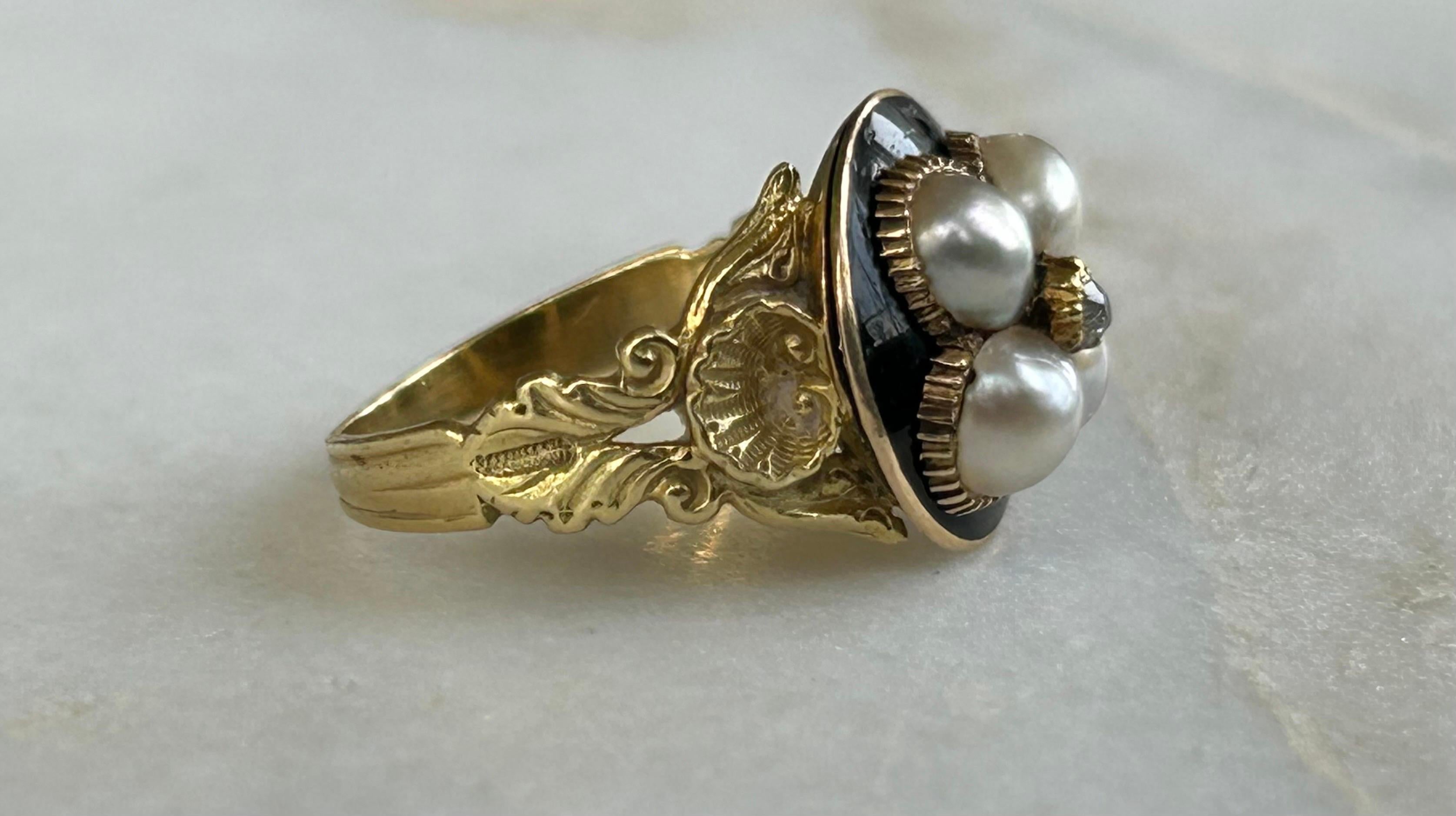 A beautiful late Georgian Natural Pearl and Enamel set mourning ring, 18ct yellow gold.
The ornate, unique long and slender shank featuring a large shell and round panel ring.
Inset to top panel with four pearls of varying shades from cream, pink