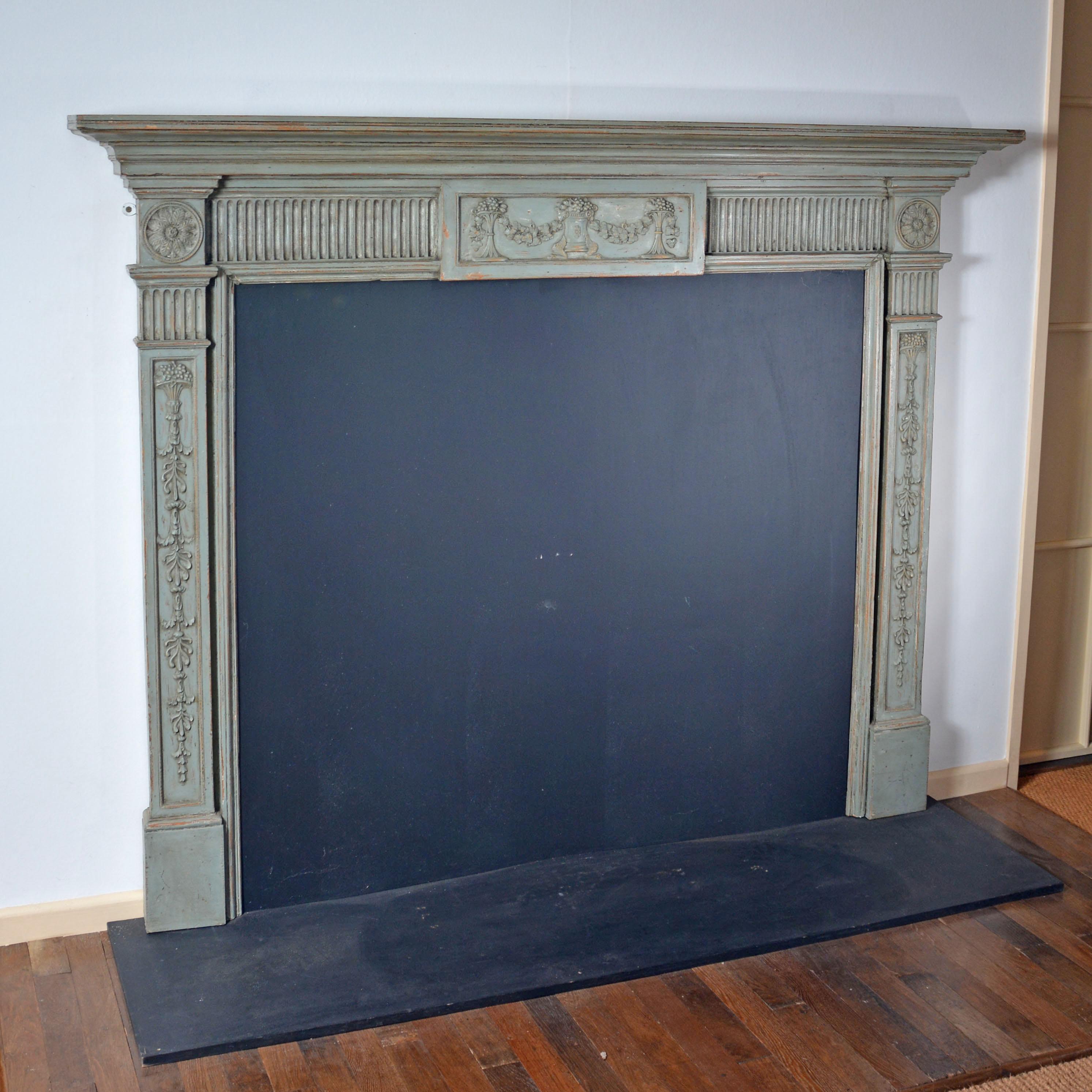Georgian neo-classical carved and painted pinewood chimney piece, the stepped mouldings beneath the mantel shelf to a gadroon carved frieze. The central tablet with garlanded classical display. To the ends, roundels of carved acanthus over jambs