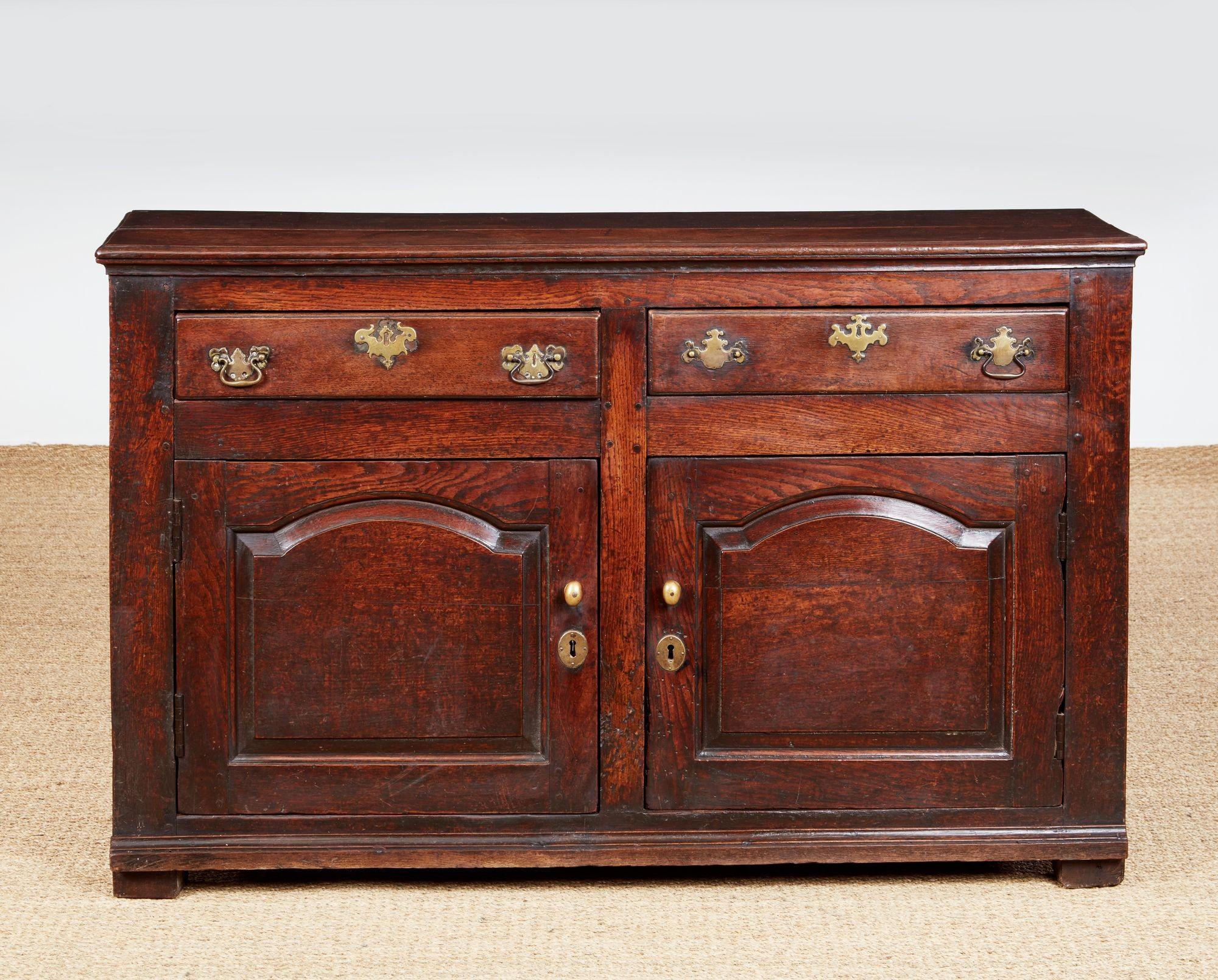 Comò basso in quercia della metà del periodo georgiano, Wales Wales, 1750 circa. Il piano a due assi con bordo modellato, sopra due cassetti e due ante di armadio con pannelli ad arco in rilievo e base modellata, poggia su piedi originali, il tutto