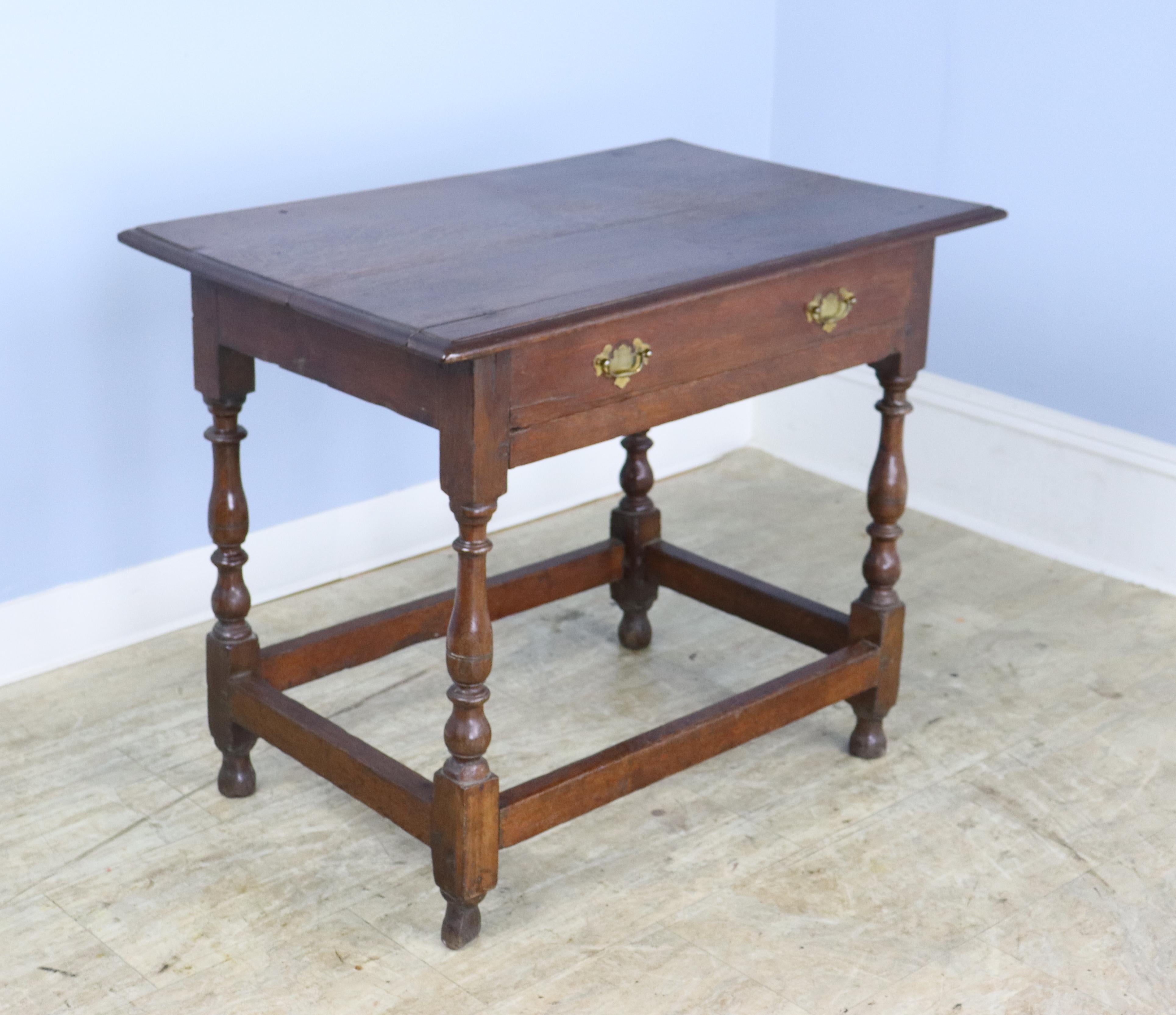 An early elegant oak side table with a pretty top with some age appropriate distress, nicely turned legs, and good brass handles.