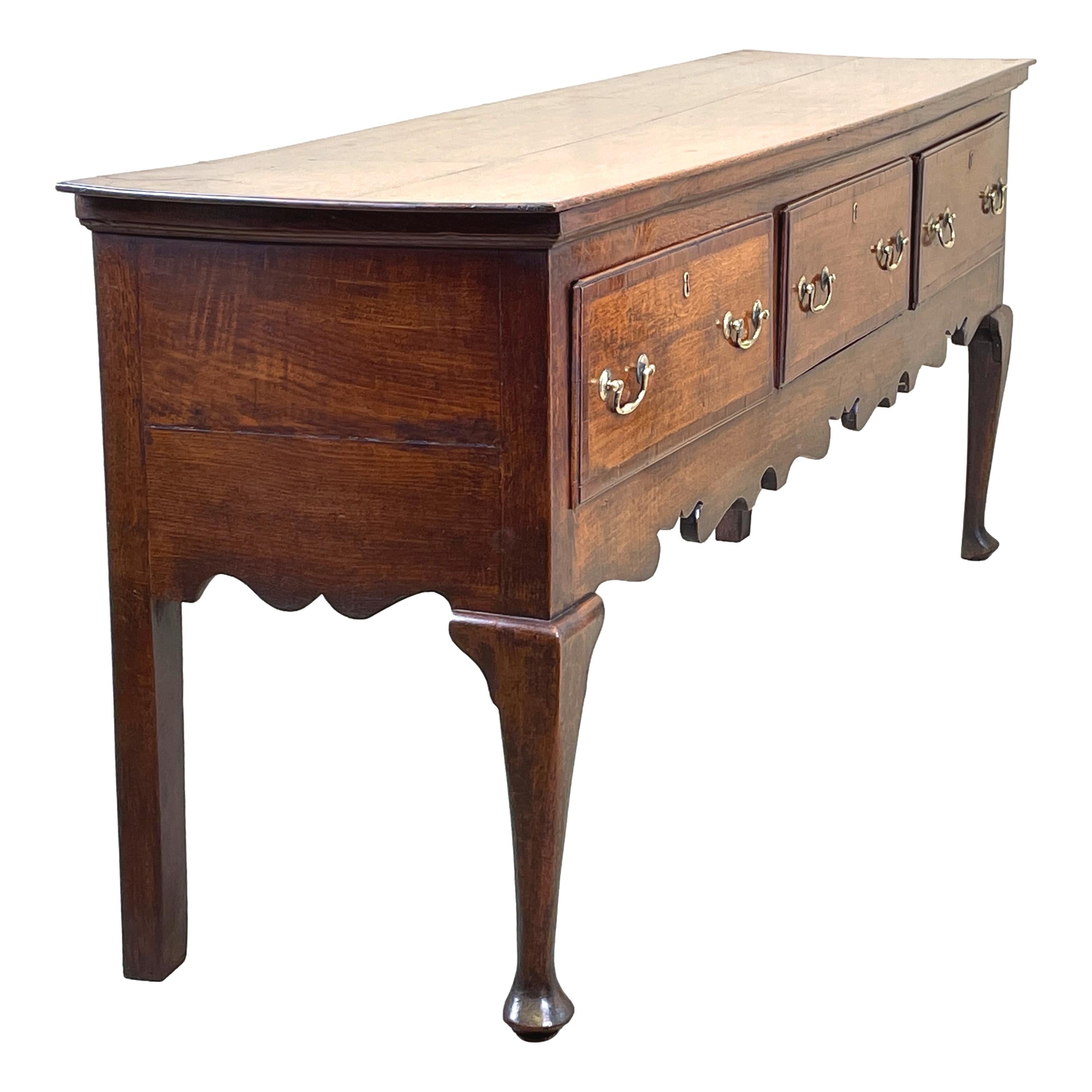 A Charming, 18th Century, Georgian Oak dresser base Of Exceptional Untouched Colour And Patina, Having Well Figured Rectangular Top Over Three Drawers, Retaining Original Brass Swan Neck Handles And Crossbanded Decoration, The Shaped Apron Raised On