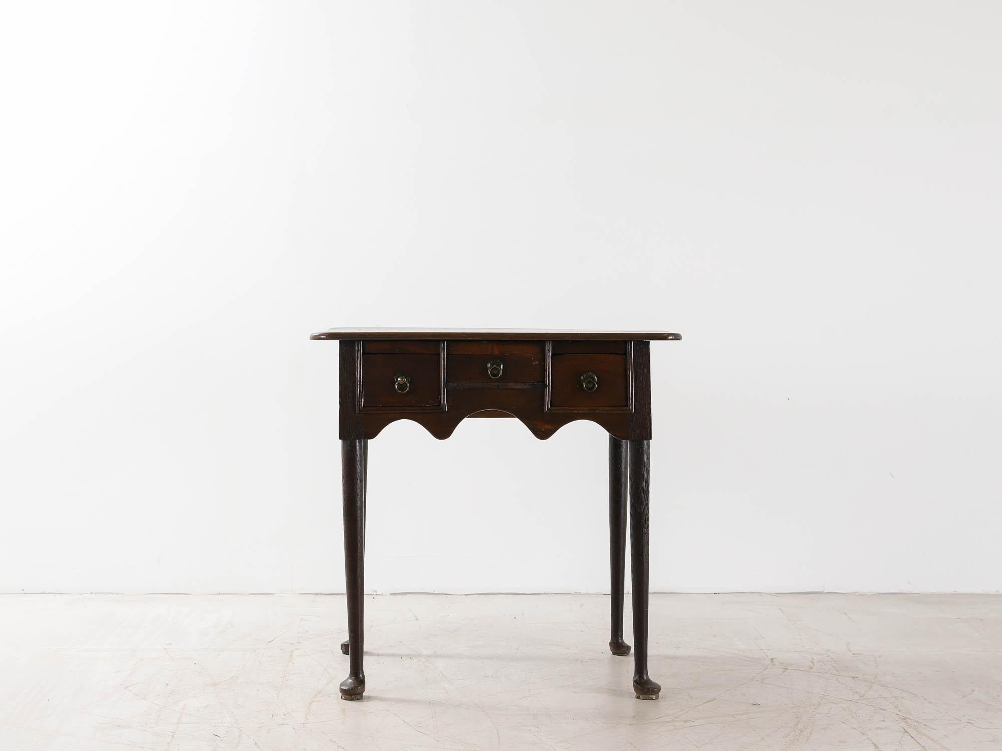 A wonderfully simple Georgian period lowboy in English oak. With a beautifully patinated top, three drawers with brass ring pulls, sitting on straight legs with pad feet.