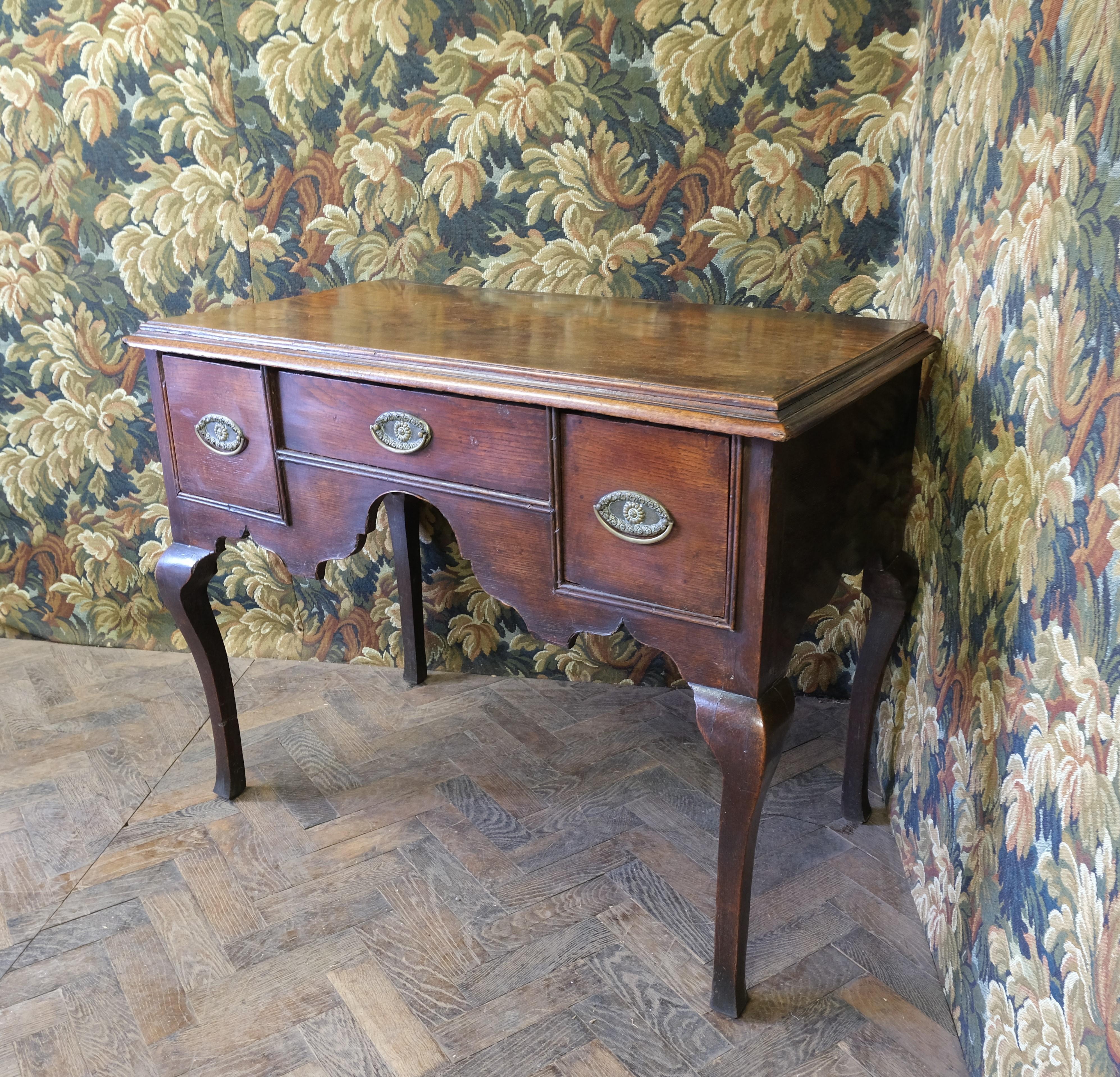 Hutton-Clarke Antiques proudly presents an exquisite mid-18th century Georgian oak lowboy. This distinguished piece showcases elegant square cabriole legs and is equipped with three drawers, complemented by a gracefully shaped apron. Its remarkable