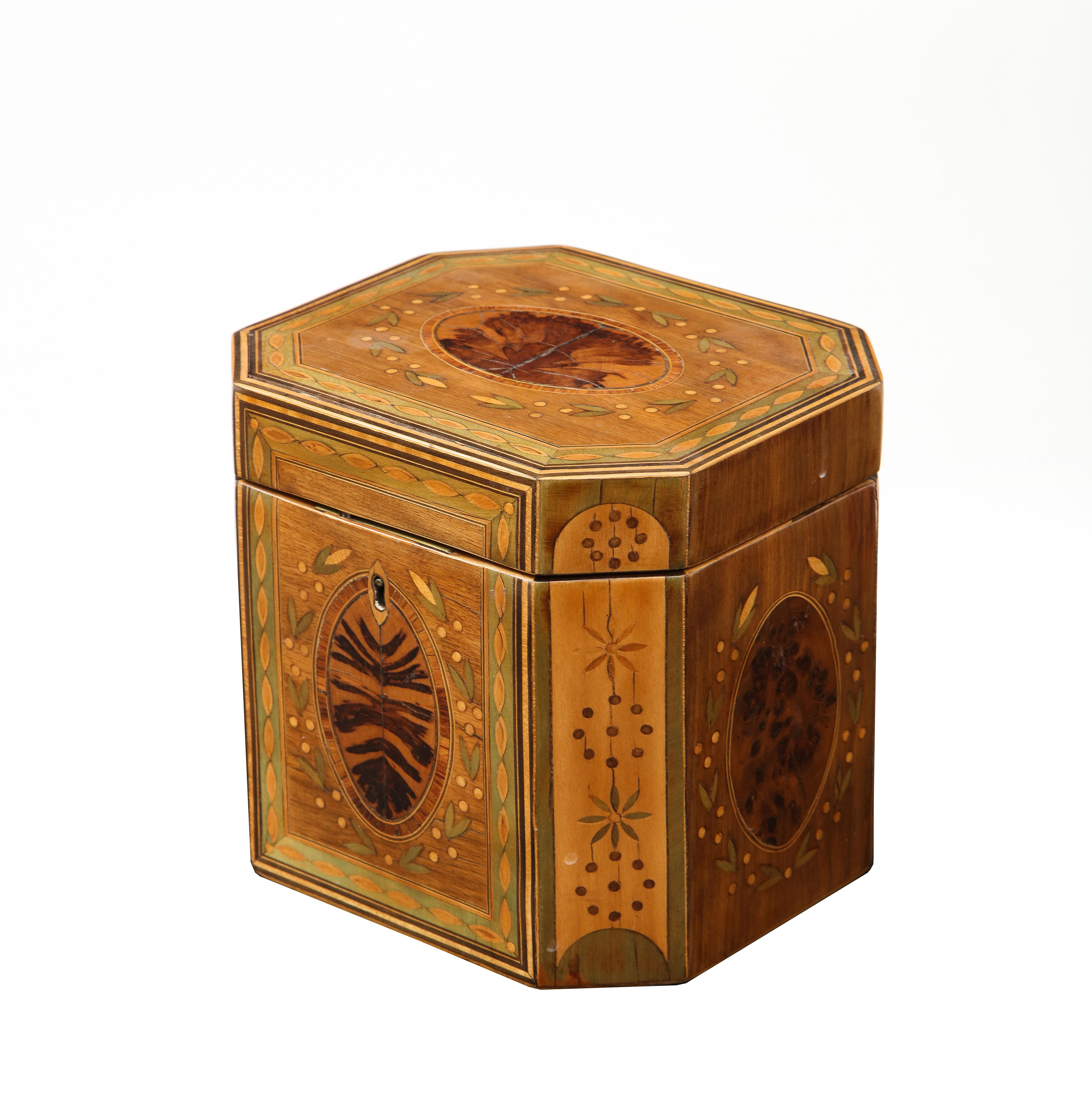 Fine boîte à thé octogonale de George III, marquetée de divers bois sur un fond de bois de lièvre, les panneaux centraux plaqués de bois de coucous et bordés de houx entourant une bande de bois de roi, des vignes et des baies marquetées sur un fond
