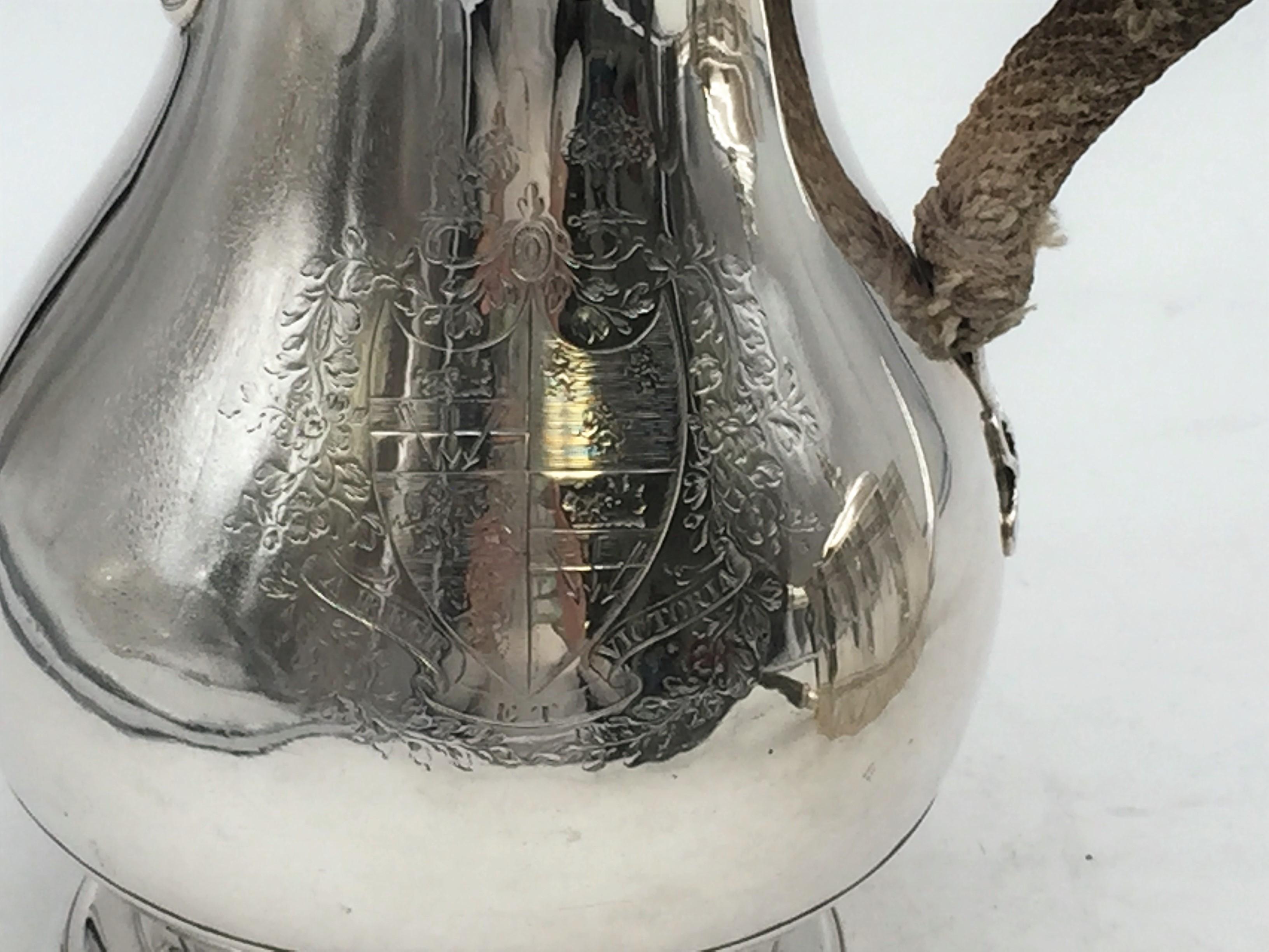 Georgian or Scottish sterling silver beer pitcher with engraved coat of arms and applied ribbon-shaped decoration by the handle. Most likely 18th century or possibly early 19th century. Measuring 7 1/2'' from handle to spout and 9'' in height.