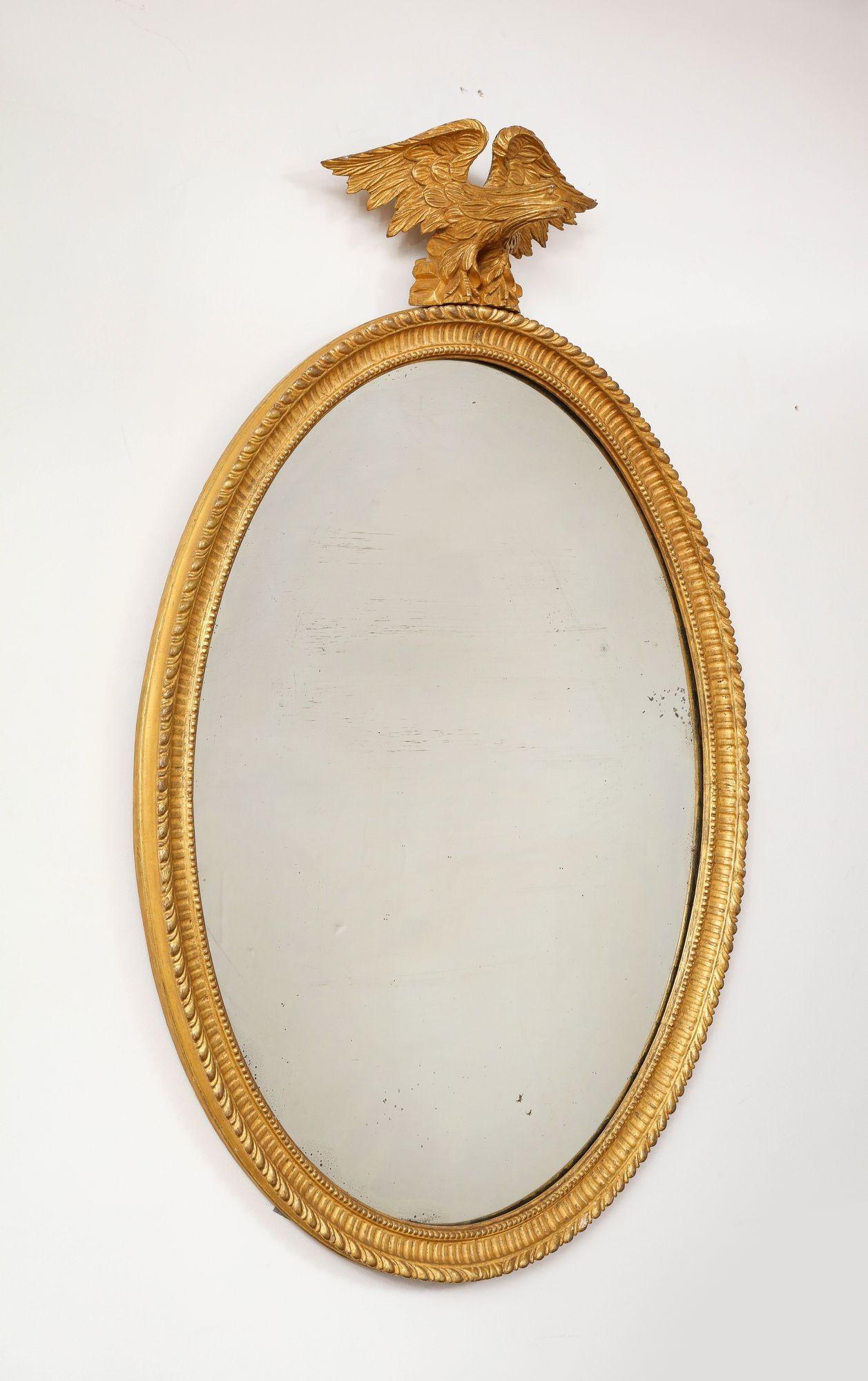 Miroir classique ovale en bois doré de George III, la crête d'aigle sculptée reposant sur une base en rocaille, surmontant un cadre ovale sculpté de godrons avec cannelures et bord intérieur perlé, conservant la plaque de miroir en verre au mercure