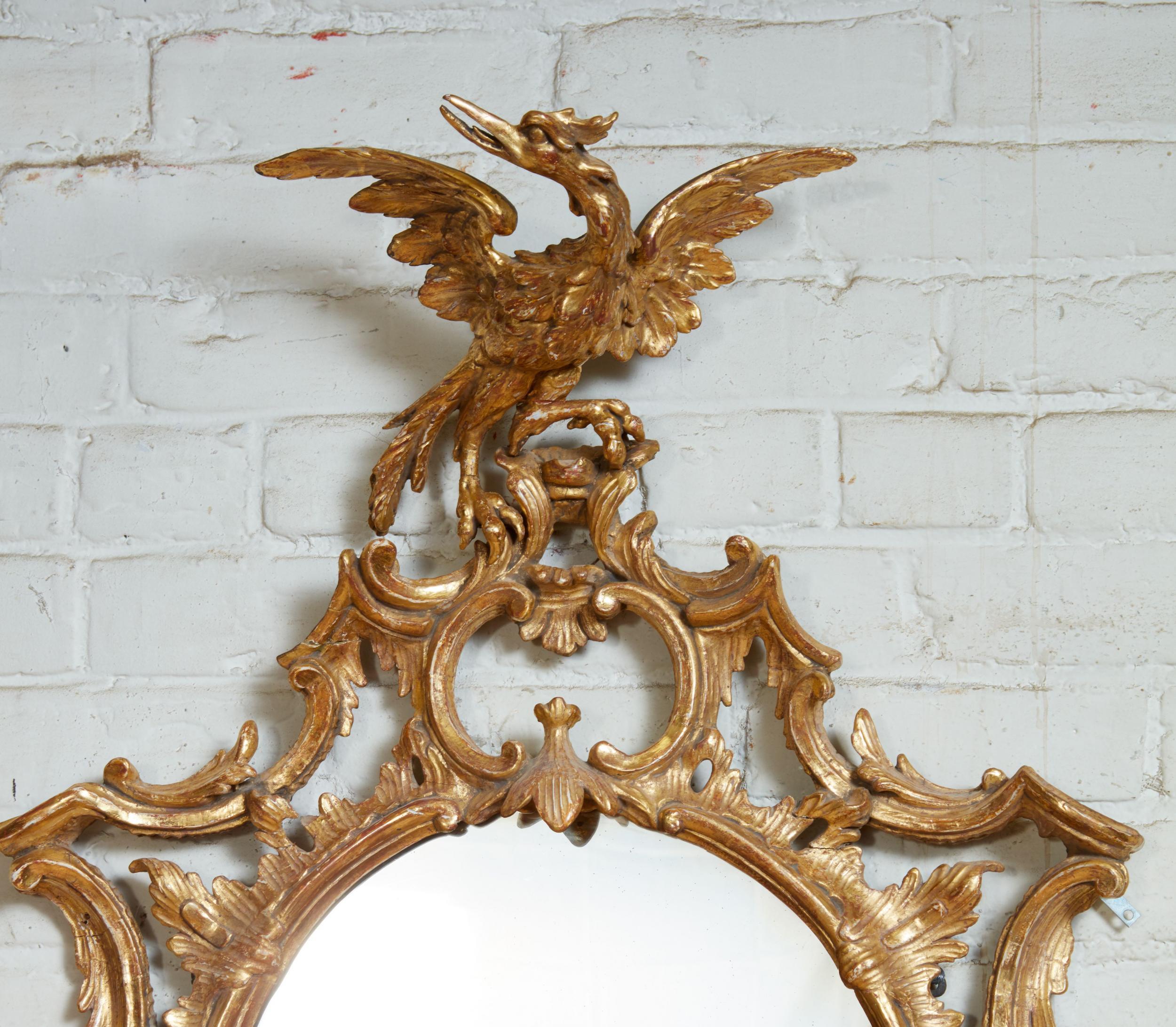 Fire George III period oval giltwood mirror, having phoenix carved crest over rococo scroll and foliate carving, the mercury glass oval plate crowned with naturalistic pagoda hood and flanked by elongated 