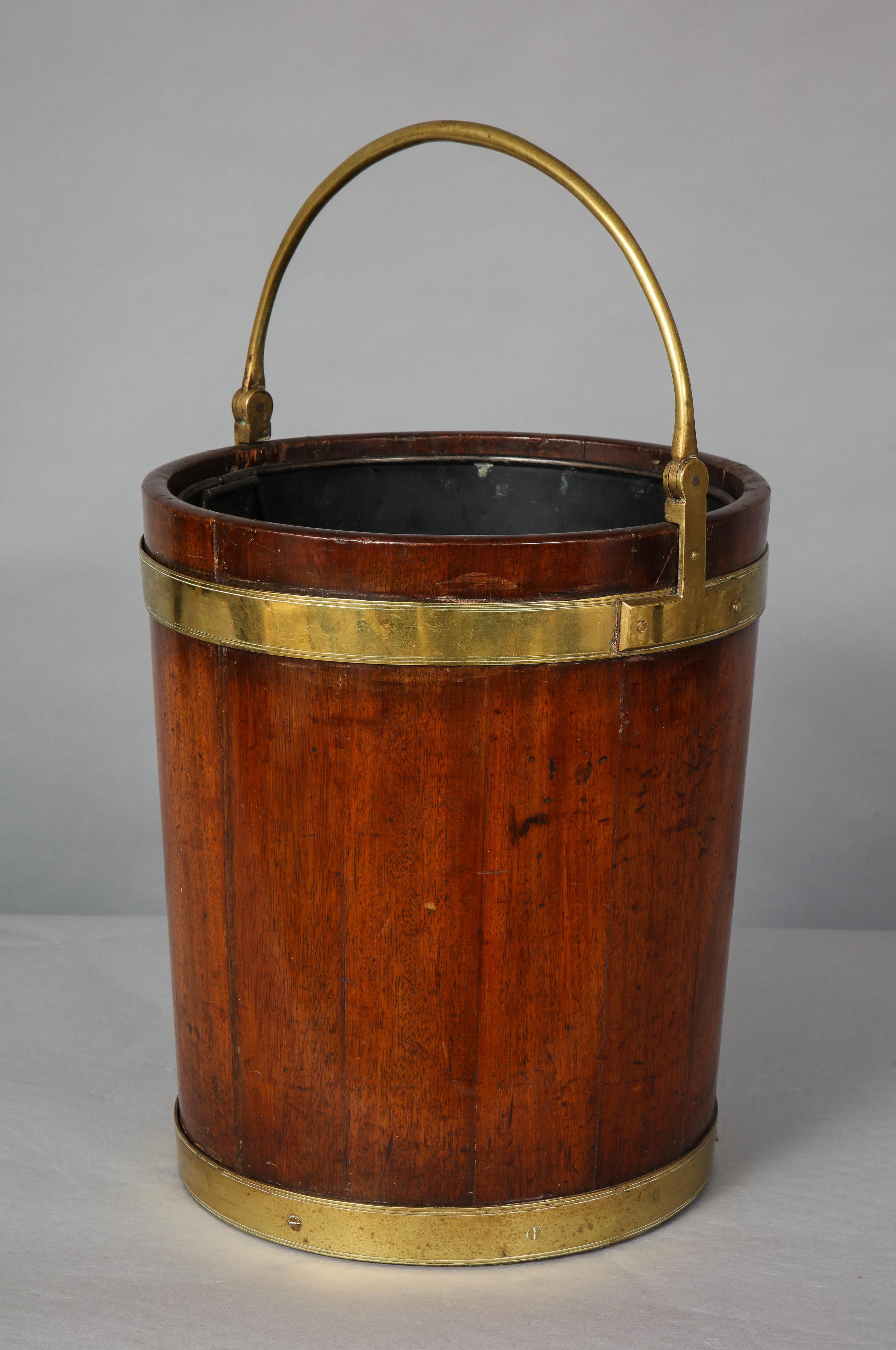 Fine English or Irish mahogany peat bucket having good heavy gauge brass handle and bands, and constructed in good and nicely patinated mahogany, circa 1800. Comes with custom metal liner. Ideal for kindling or as waste paper basket.

Height below