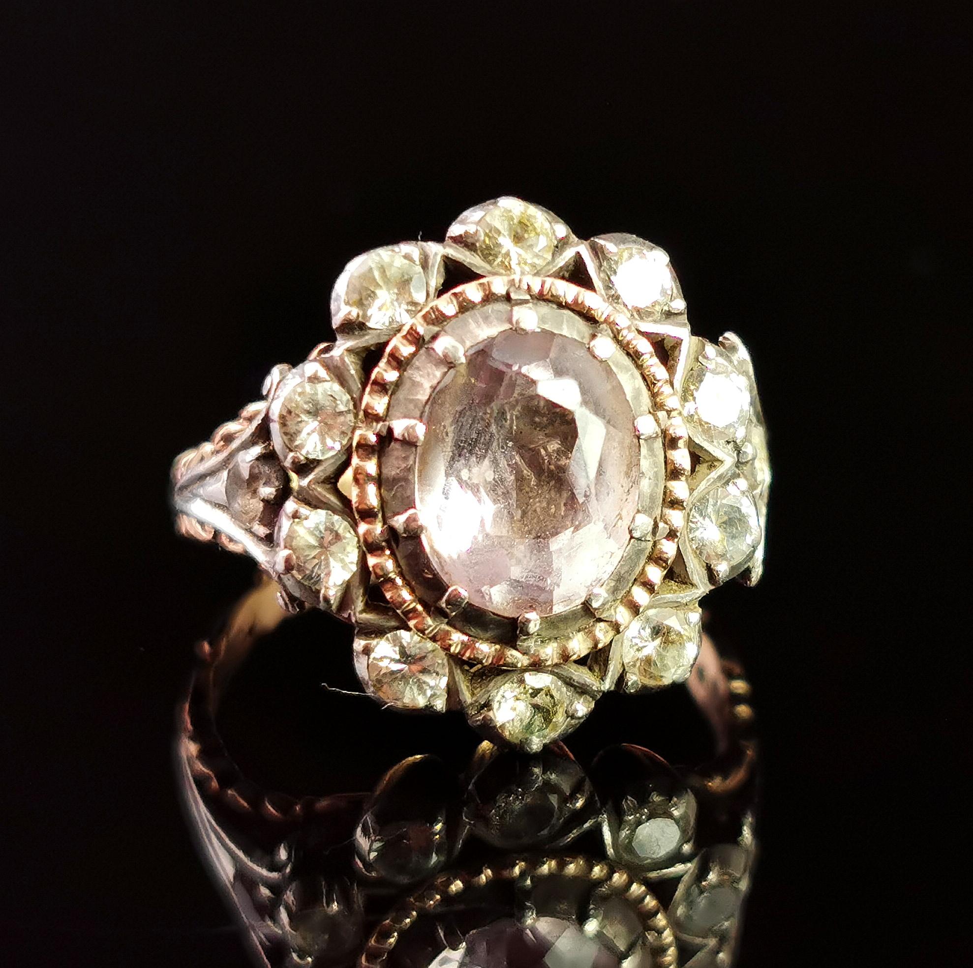 A stunning antique Georgian era pink topaz and paste cluster ring.

This is a very grand ring with a huge oval cut light pink topaz to the centre surrounded by a gold bezel frame and a halo of sparkling old cut paste stones in a floral design.

The