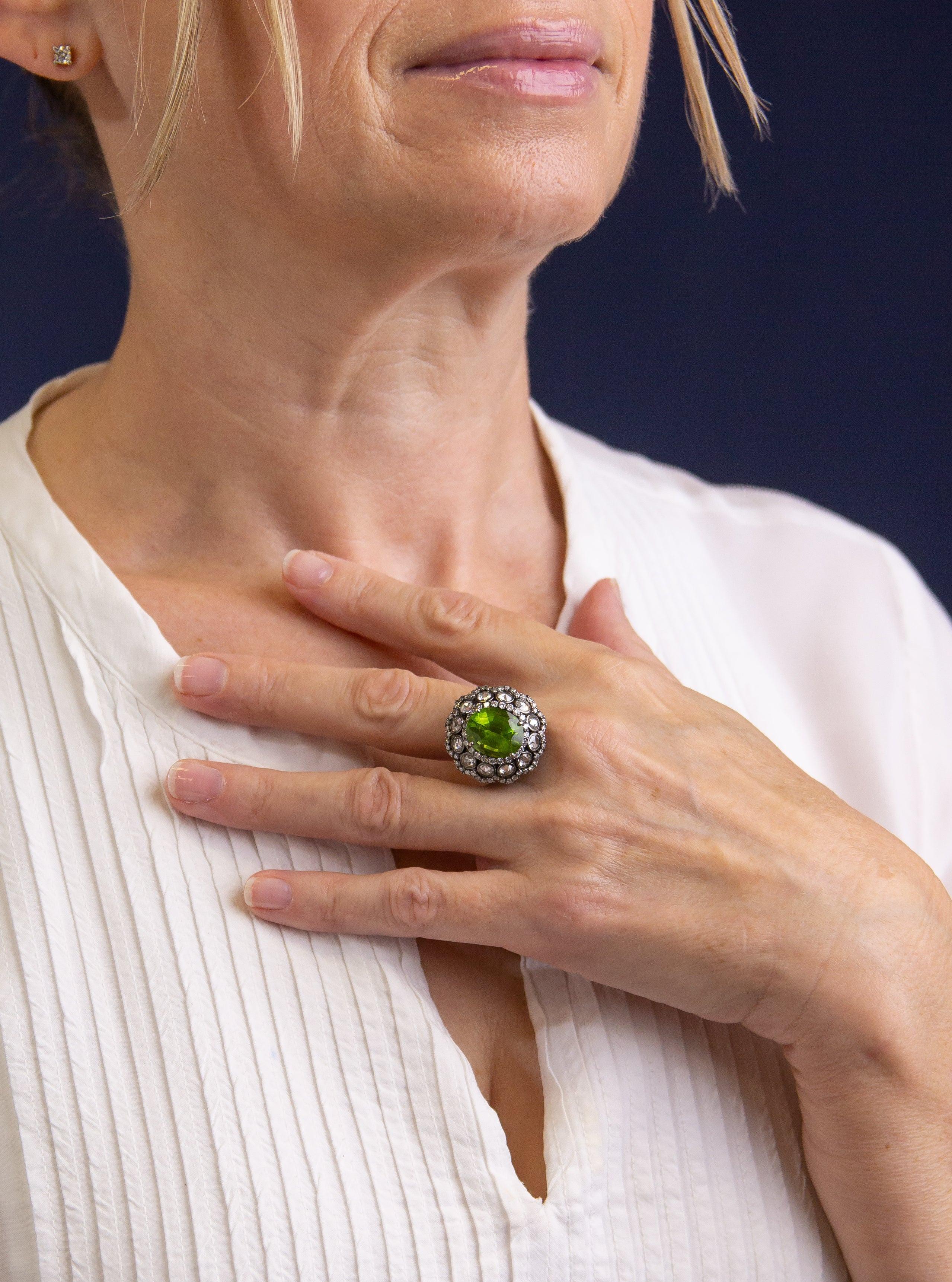 This rather attractive peridot and diamond ring has been made to reference jewellery of the Georgian period. The rhodium plated blackened frame of the ring is crafted from 18 karat white gold and centres to the top with an oval cut peridot weighing
