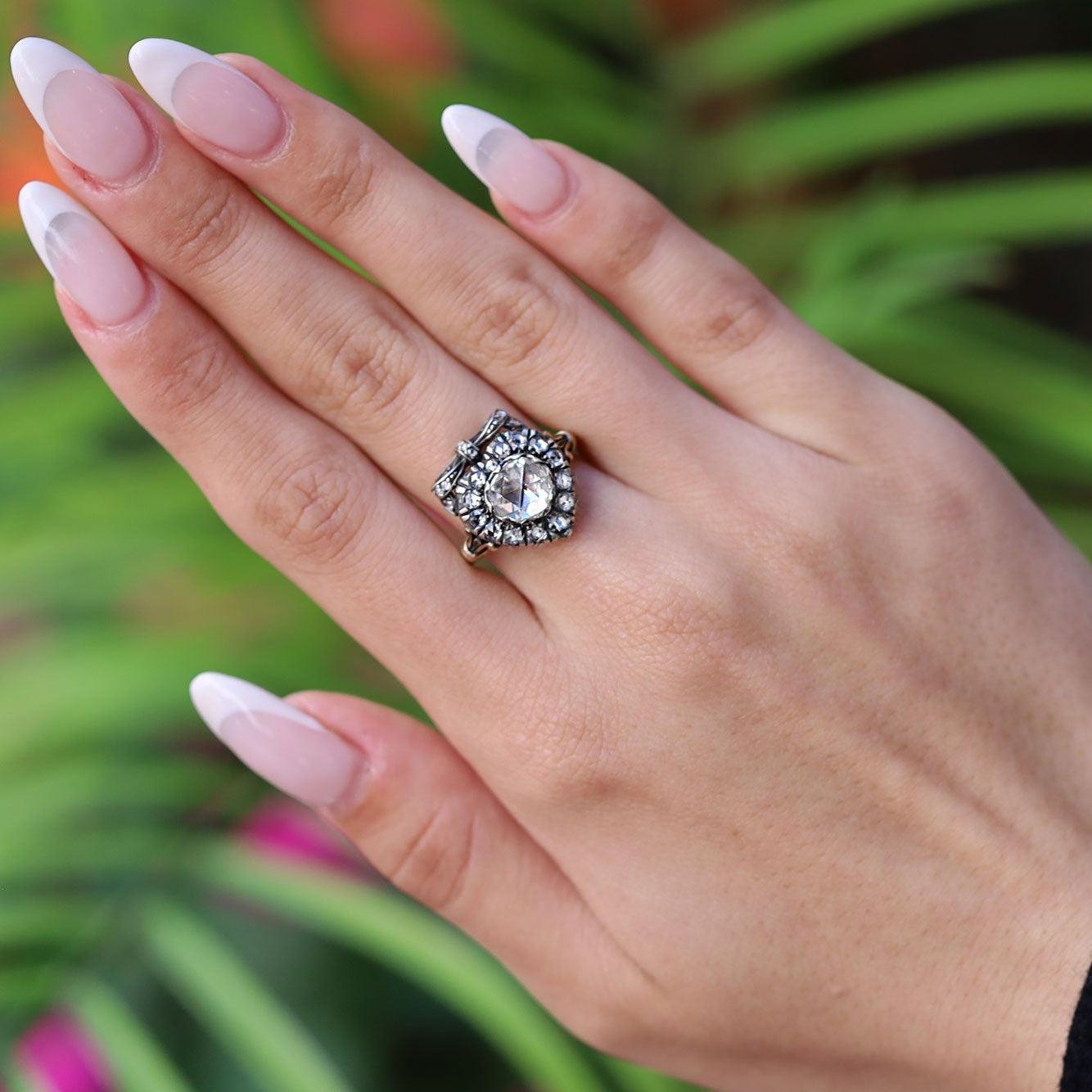 A most romantic Georgian style rose cut diamond engagement ring. The heart motif adorned with a delightful bow and centered by a charming, 0.93 carat antique diamond glimmering with a unique sparkle. Meticulously hand crafted of 18k rose gold and