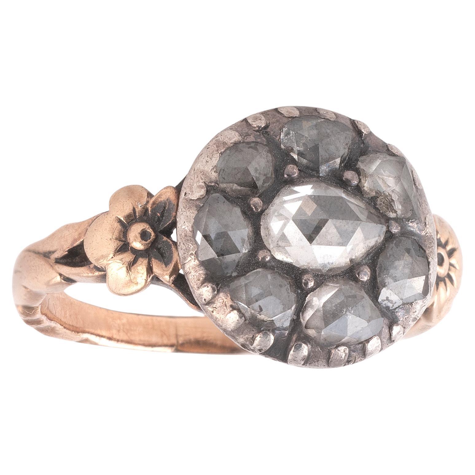 The round rose-cut diamond surrounded by small rose cuts border, within foiled closed-back settings, to trifurcated fleur-de-lys shoulders and a reeded hoop, mounted in silver and gold.
Top size 12mm

Weight: 3.68g

Size 4