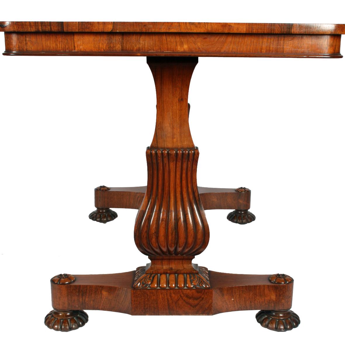 An early 19th century George IV rosewood veneered library table with a twin support base.

The table has a pair of fabulous supports at each end comprising a platform lifted on carved rosewood bun feet with concealed casters.

The two platforms