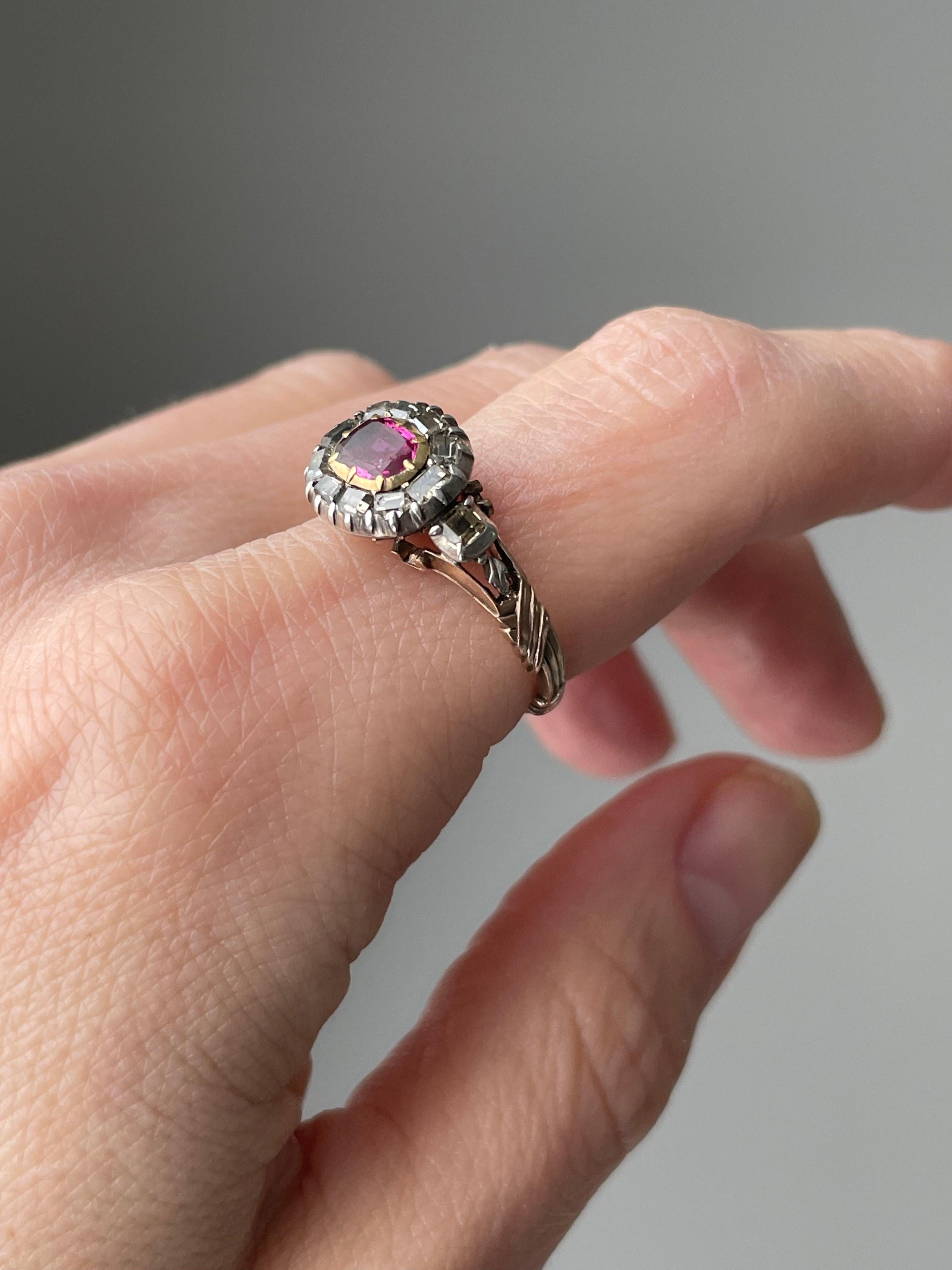 This exceptionally lovely Georgian ring centers on a vibrant raspberry red ruby framed in a halo of mirror like table-cut diamonds. The shoulders are beautifully decorated with stylized cornucopia, each sprouting a tiny diamond rosette, symbolic of