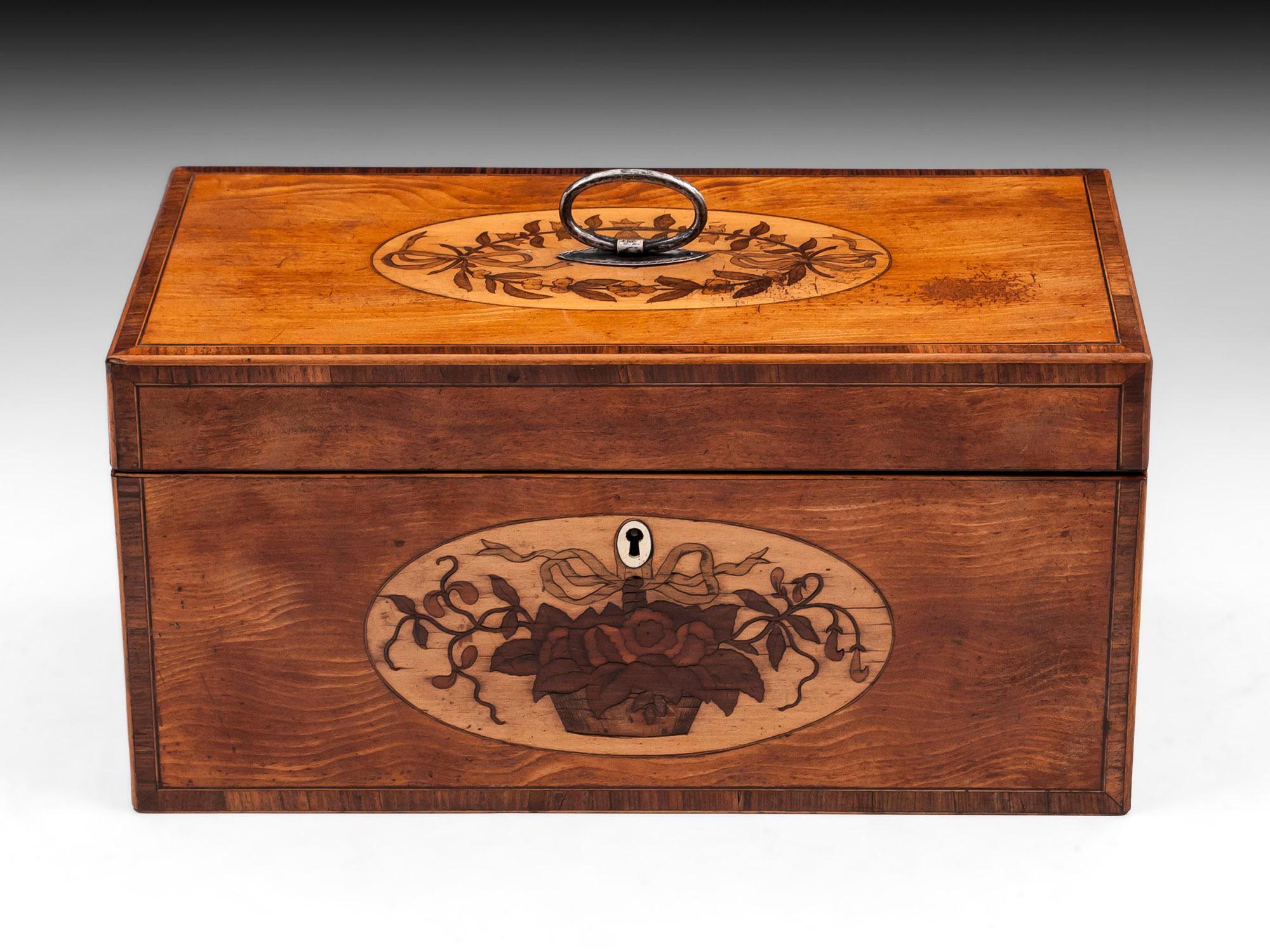 Antique satinwood tea chest with an oval inlay to the front depicting a floral basket with a bone escutcheon. The top has an oval floral inlay framing the engraved silver plated handle. The edge is crossbanded with a kingwood and boxwood banding.