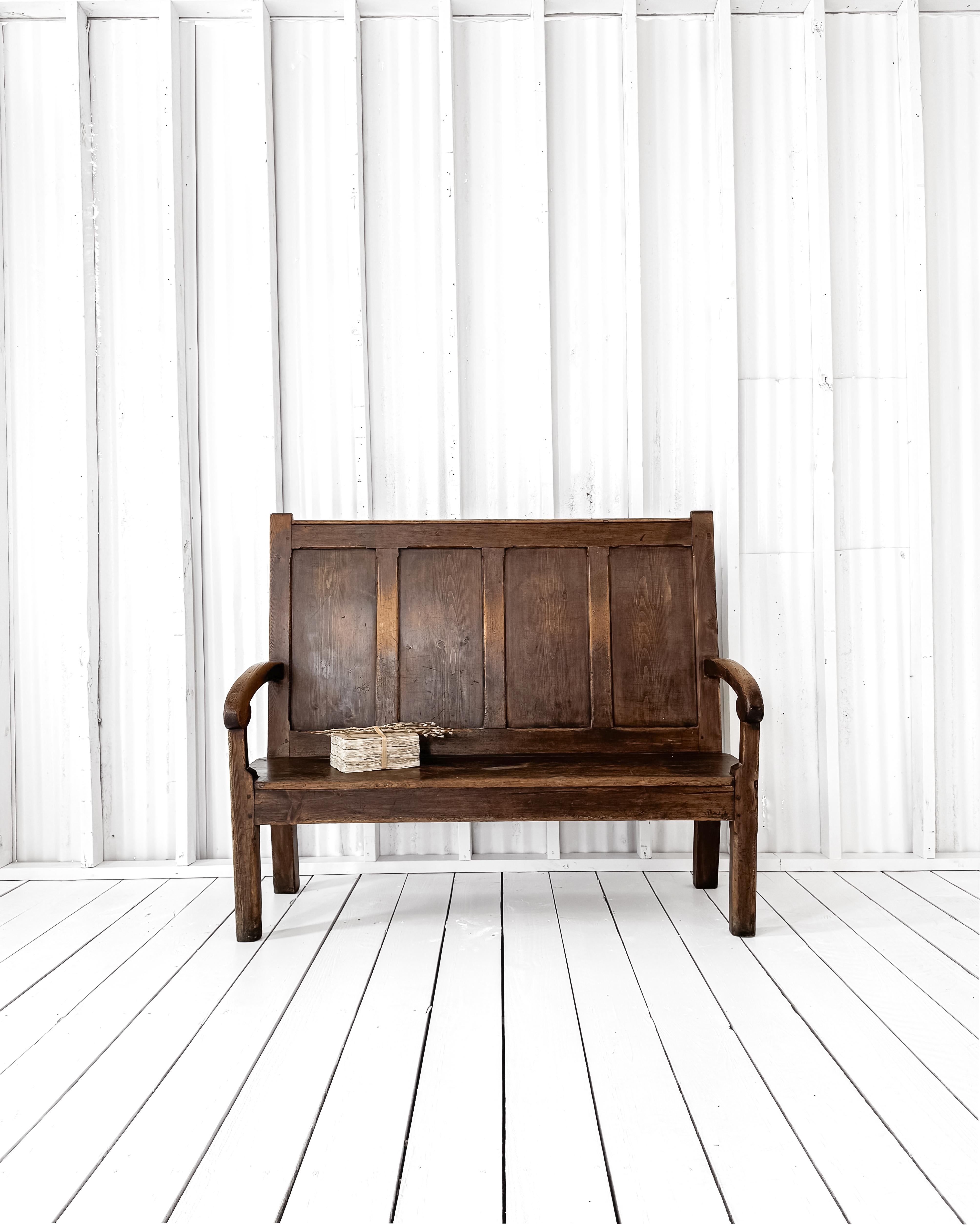 A handsome 19th-century English pine settle with a beautiful patinated finish. The masculine lines of the high fielded panel back are softened by the gracefulness of the slightly curved arms. Pegged construction, a wonderful dark stain, and simple