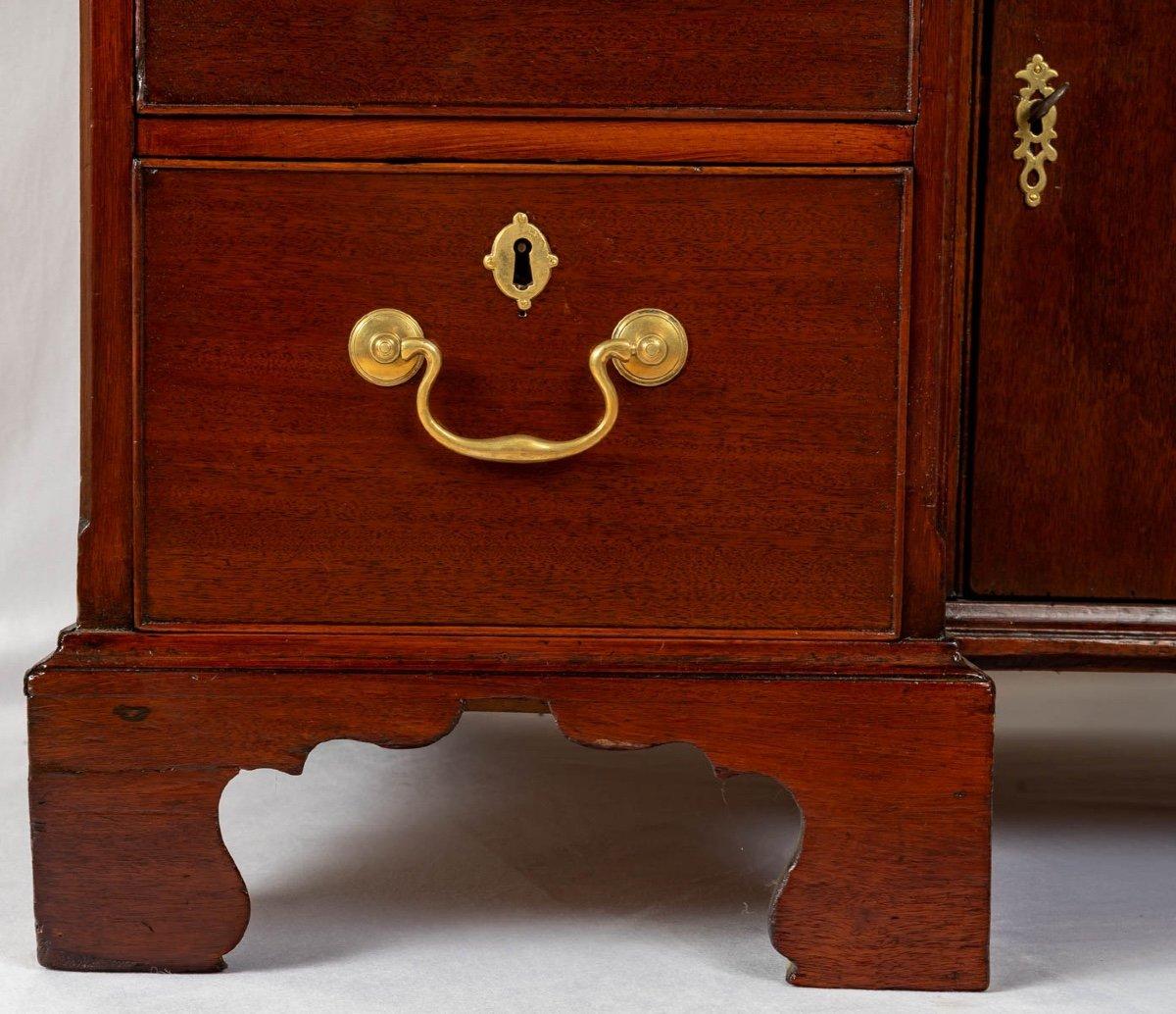 A small Georgian period mahogany knee-hole desk with blue leather sliding writing surface. 
It has a single full width central drawer topped by a hinged cupboard door in the knee hole, flanked on either side by three graduated drawers on raised