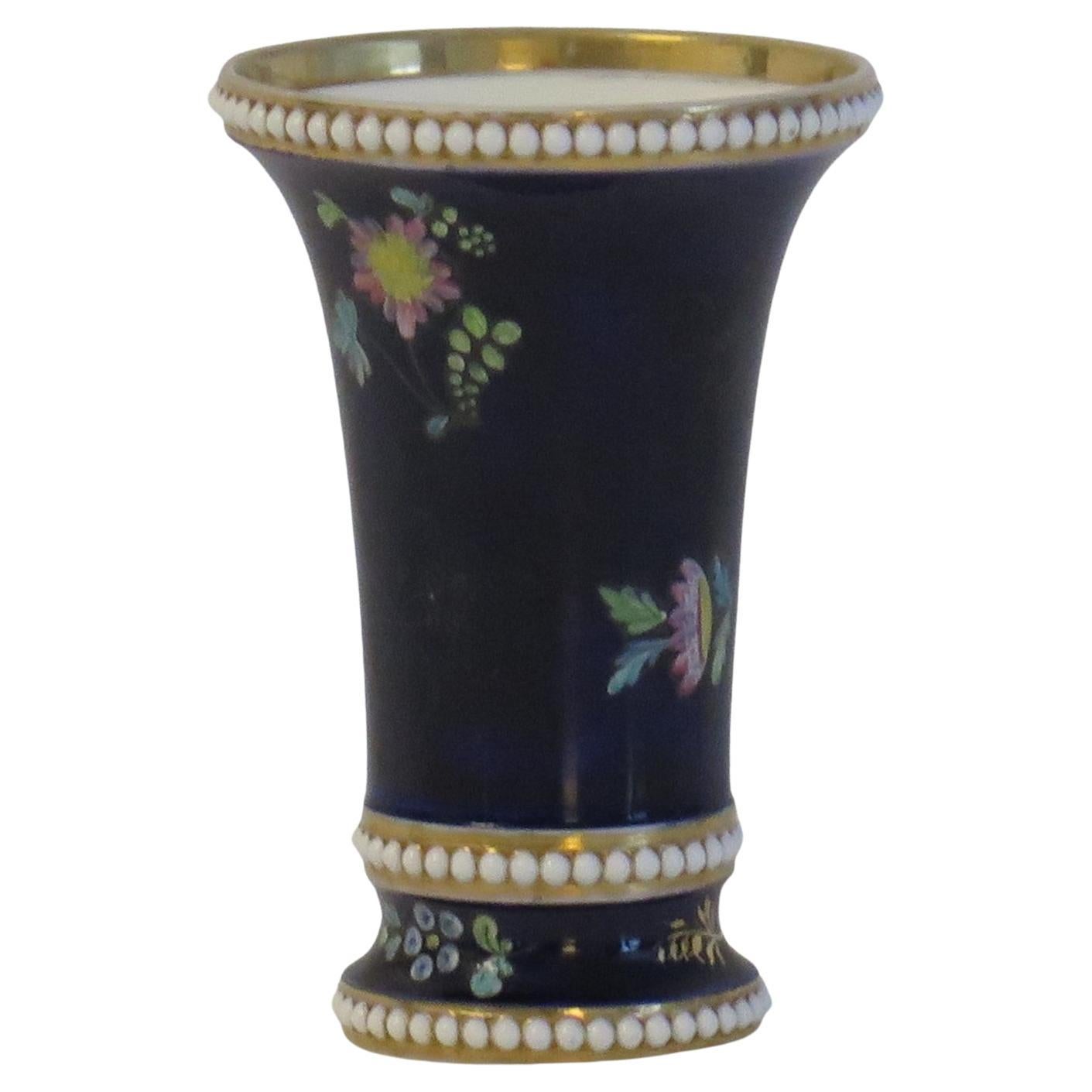 This is a small spill vase, hand painted in enamelled & gilded floral sprigs against a Mazarine blue ground, made by Josiah Spode, Stoke on Trent, England and dating to circa 1810.

The vase is well potted with a tapering shape and beaded