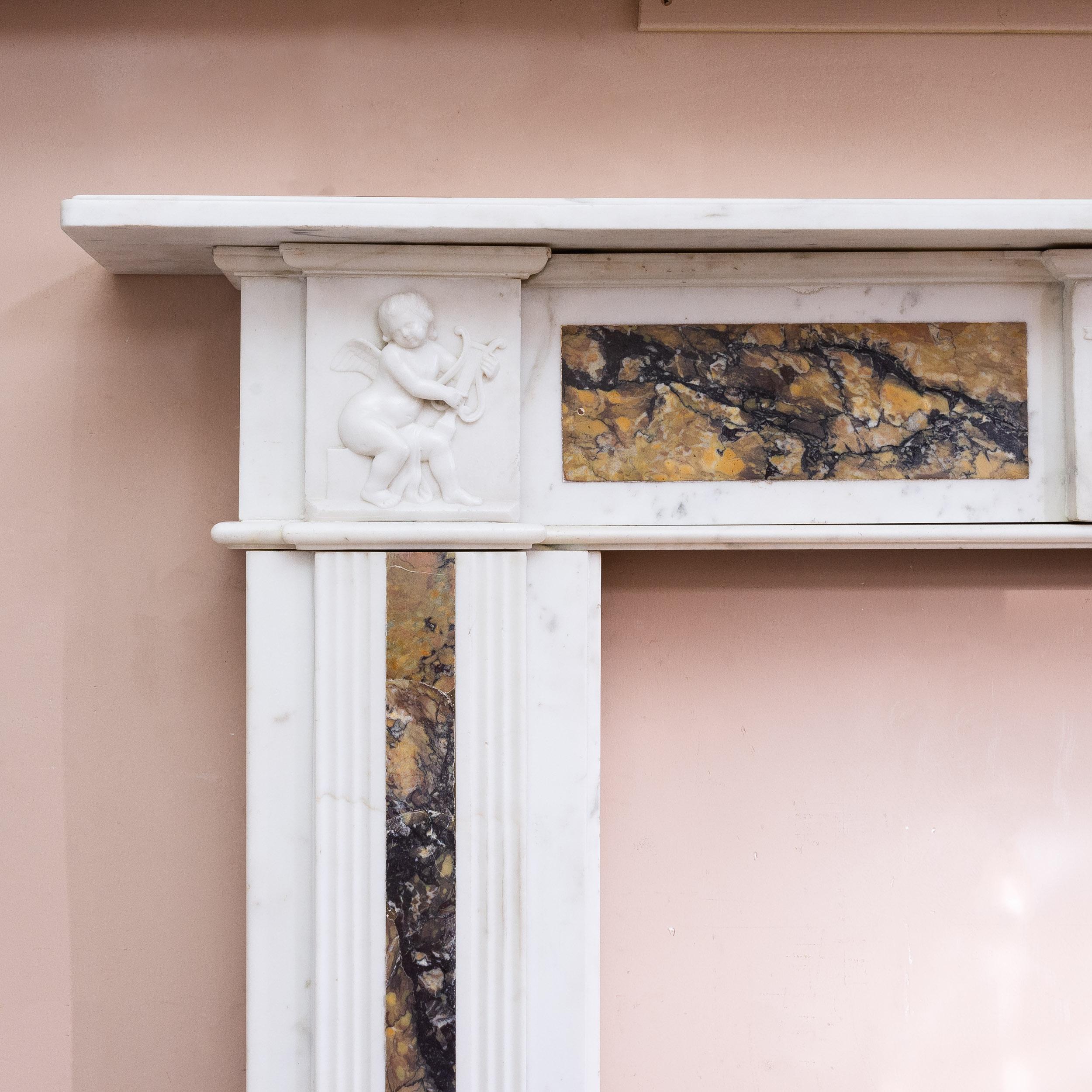 A late Georgian Statuary and Convent Sienna marble fireplace, circa 1800,
the shelf with a simple mould above frieze with plaque centred by a female mask, the corner blocks of putti above fluted panel jambs, the whole inset with panels of