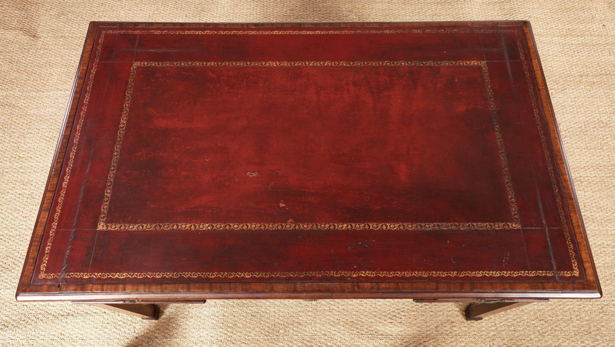 A Georgian mahogany writing table with burgundy leather inset top over three-drawered apron with central drawer stepped above two side drawers, standing on four bold square section legs with foot moldings. Fine craftsmanship, including gilt tooling