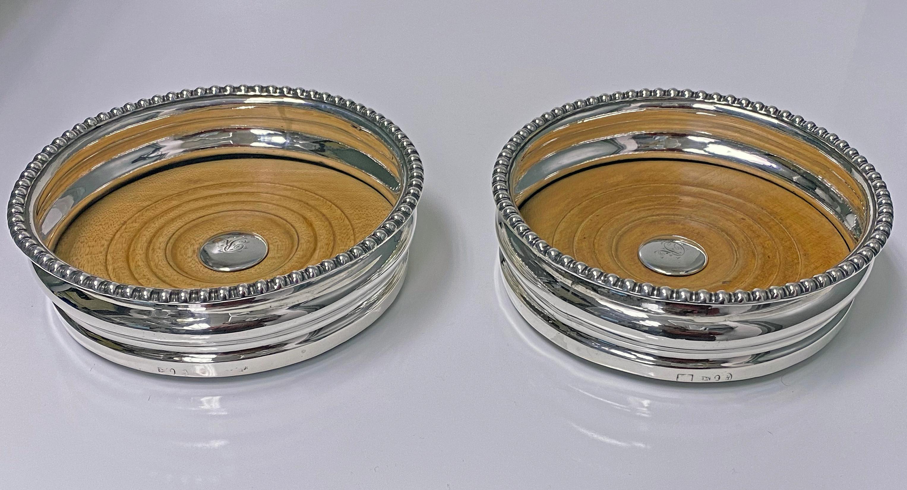 Antique Georgian sterling silver wine coasters, city of Sheffield 1810, Thomas Blagden. Each of circular rounded shaped form, plain ribbed bodies, gadroon borders. Original turned wood bases, central silver bosses with letter R. Baize to undersides.