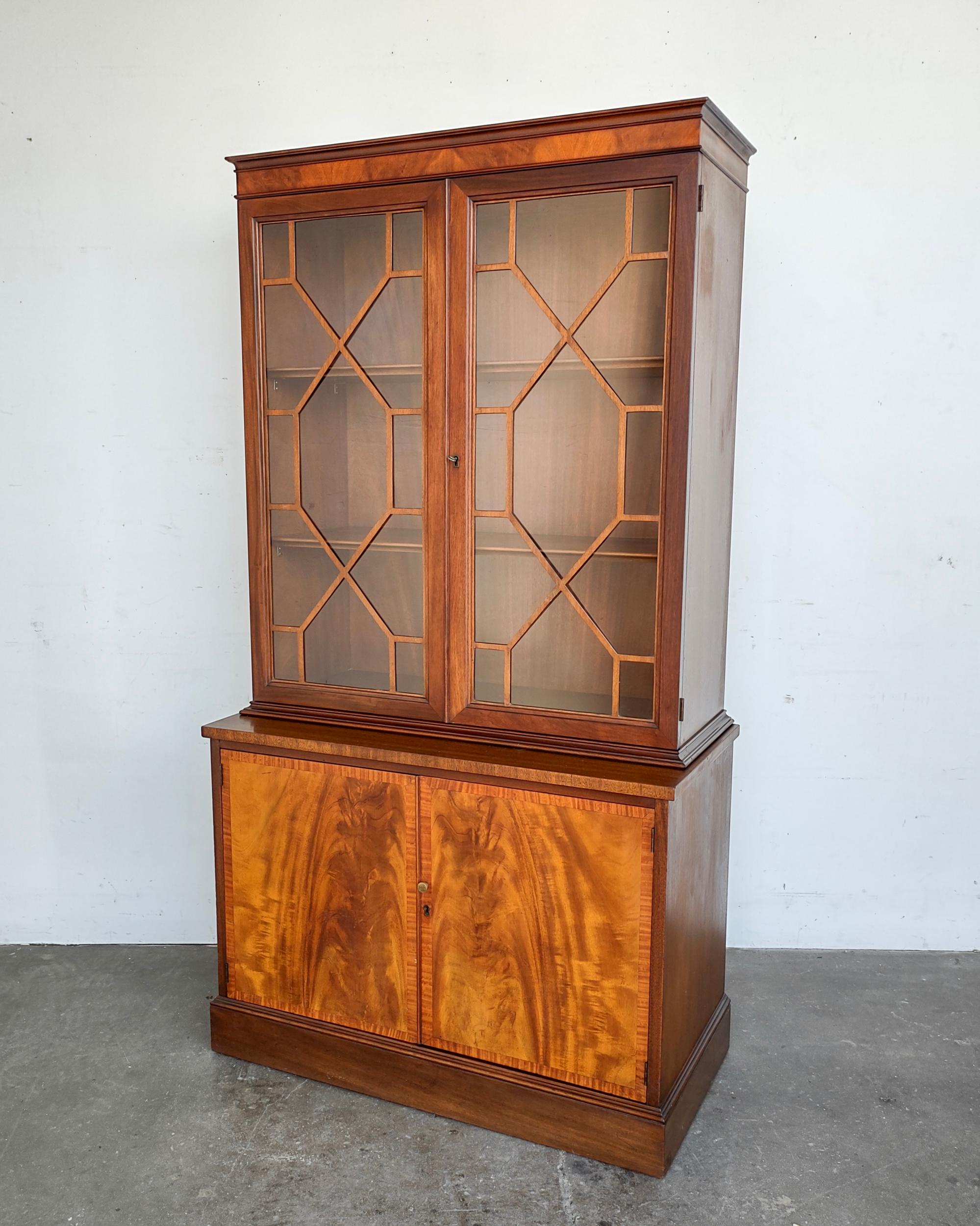 Flame mahogany Georgian style bookcase cabinet. Gorgeous wood grain covering entire body. Upper cabinet features glass doors with cutout wood pattern, inside had two removable shelves. Lower cabinet lock hardware missing, inside one removable shelf.