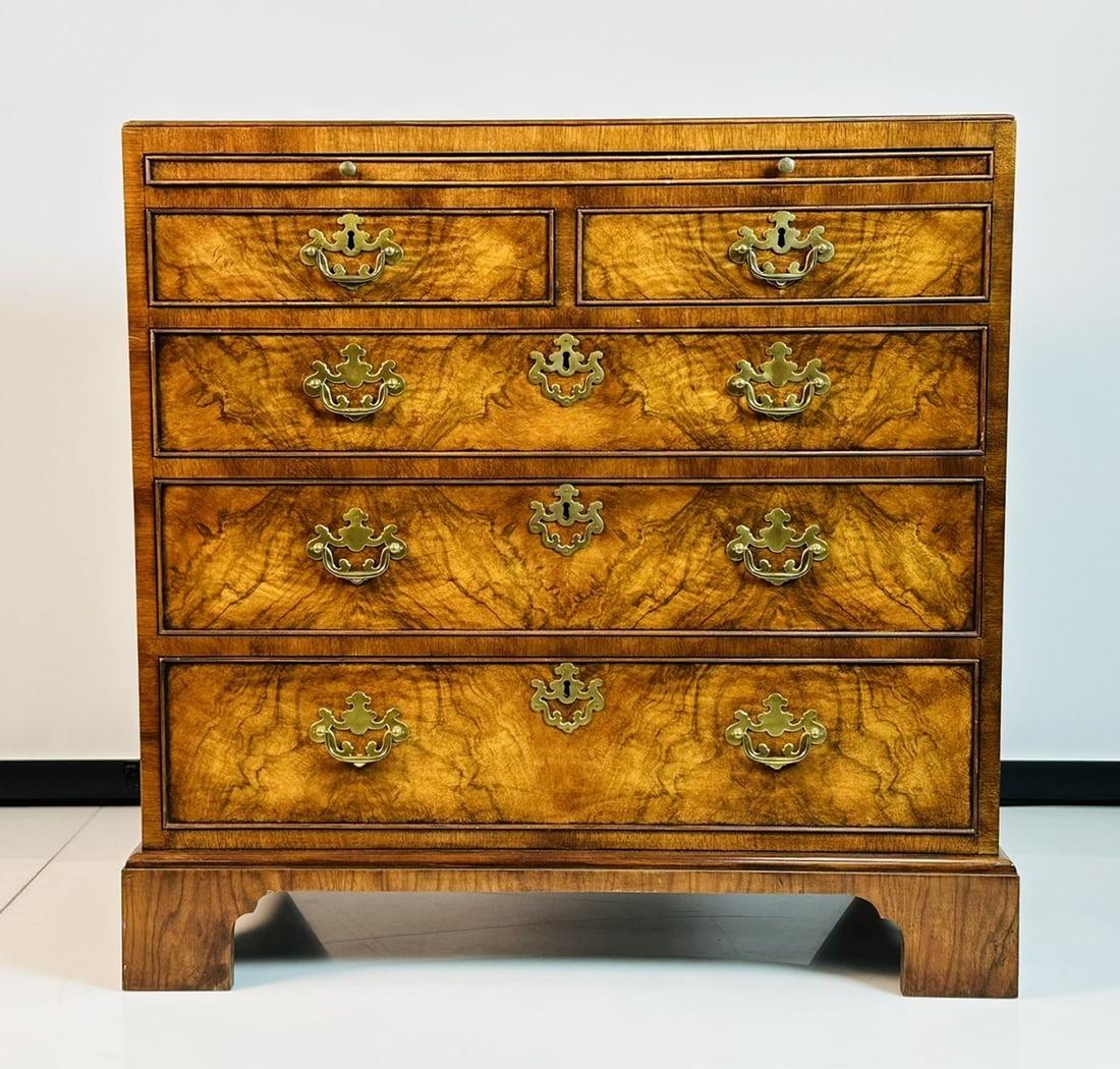 Beautiful chest of drawers in the Georgian style having a beautiful wood grain, brass hardware and a pullout shelf with tooled leather and gold details. 
 
 The piece was designed and manufactured in the USA by Baker Furniture as part of the