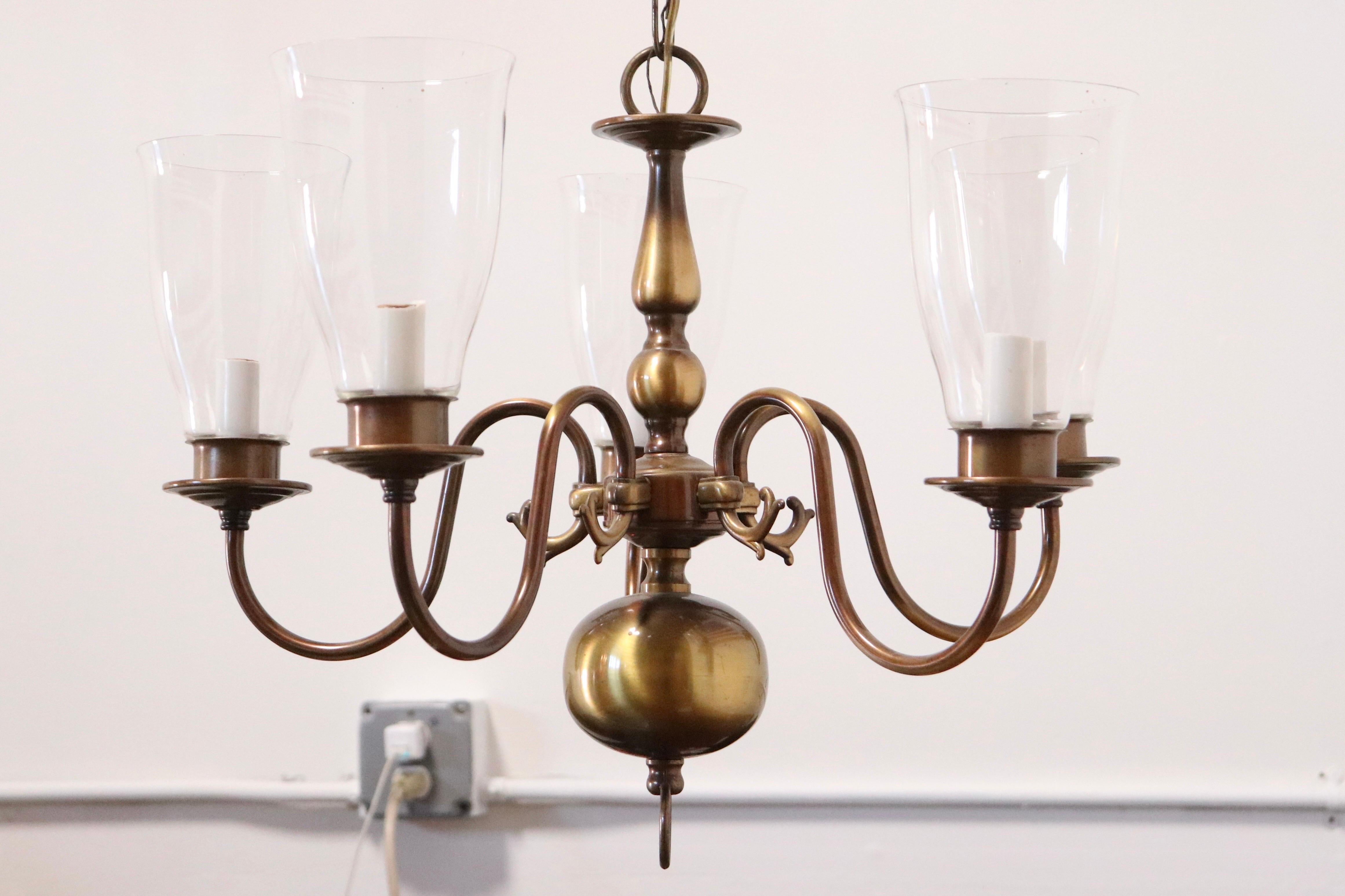 Georgian-style medium-size chandelier with 5 electrified arms holding clear glass hurricane shades, in polished brass.

Features classic English design elements including urn shape in the post and large globe below, with each curved scroll arm